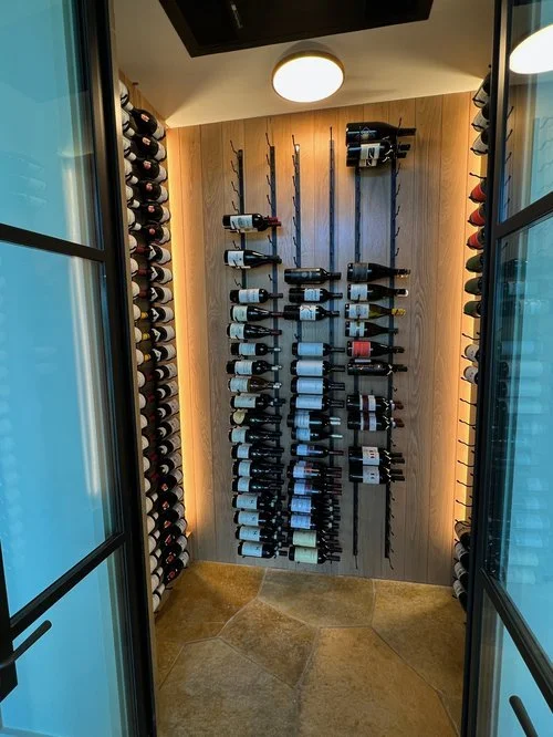 Wine bottles stored on vertical racks inside a small closet with glass doors, beige walls, and a ceiling light.