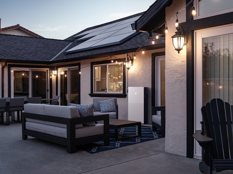 Outdoor patio area of a house with string lights, modern furniture, and solar panels on the roof during twilight.