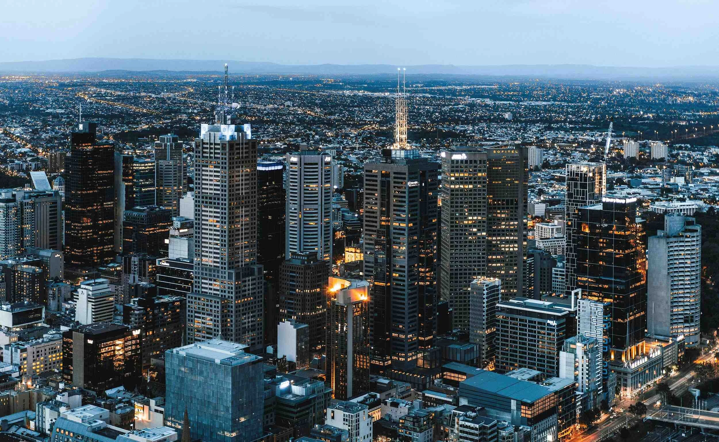Aerial view of a city skyline at dusk with tall skyscrapers and city lights.