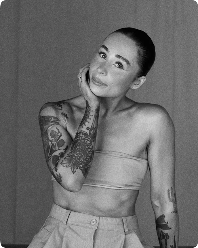 Portrait of Cassie Tierney Clarke, digital creator represented by Moth Management. A woman with dark hair pulled back, tattoos on her right arm, wearing a strapless top and high-waisted pants, looking at the camera with a slight smile.