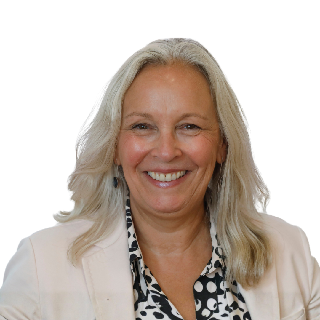 Gillian Hadfield with shoulder-length gray hair smiling in front of a plain white background, wearing a light-colored blazer and a black-and-white polka-dot blouse.