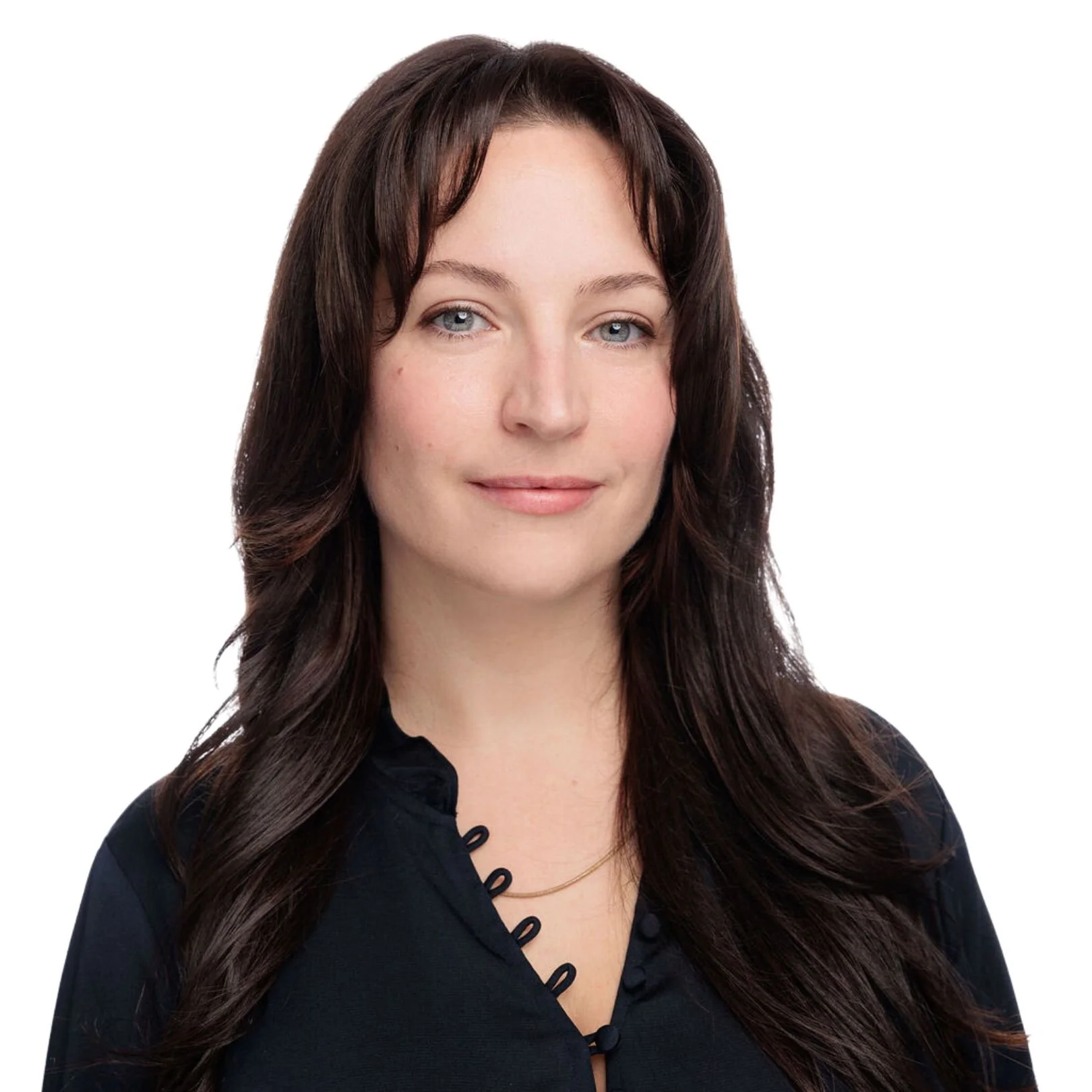 A portrait of Carly Tryens with long dark hair, blue eyes, and light skin, wearing a black top with button details and a gold necklace, smiling softly against a white background.
