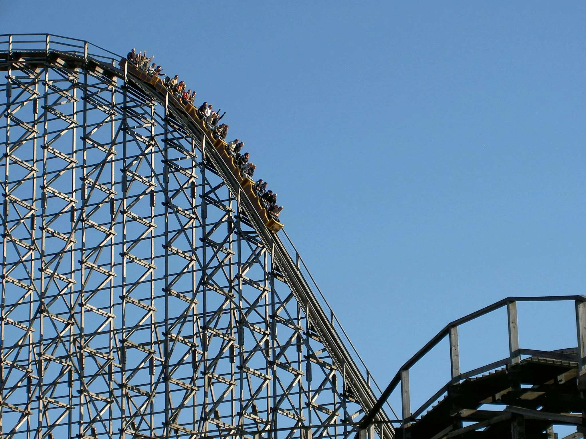 Achterbahn mit vielen Passagieren in einem Freizeitpark gegen den blauen Himmel.
