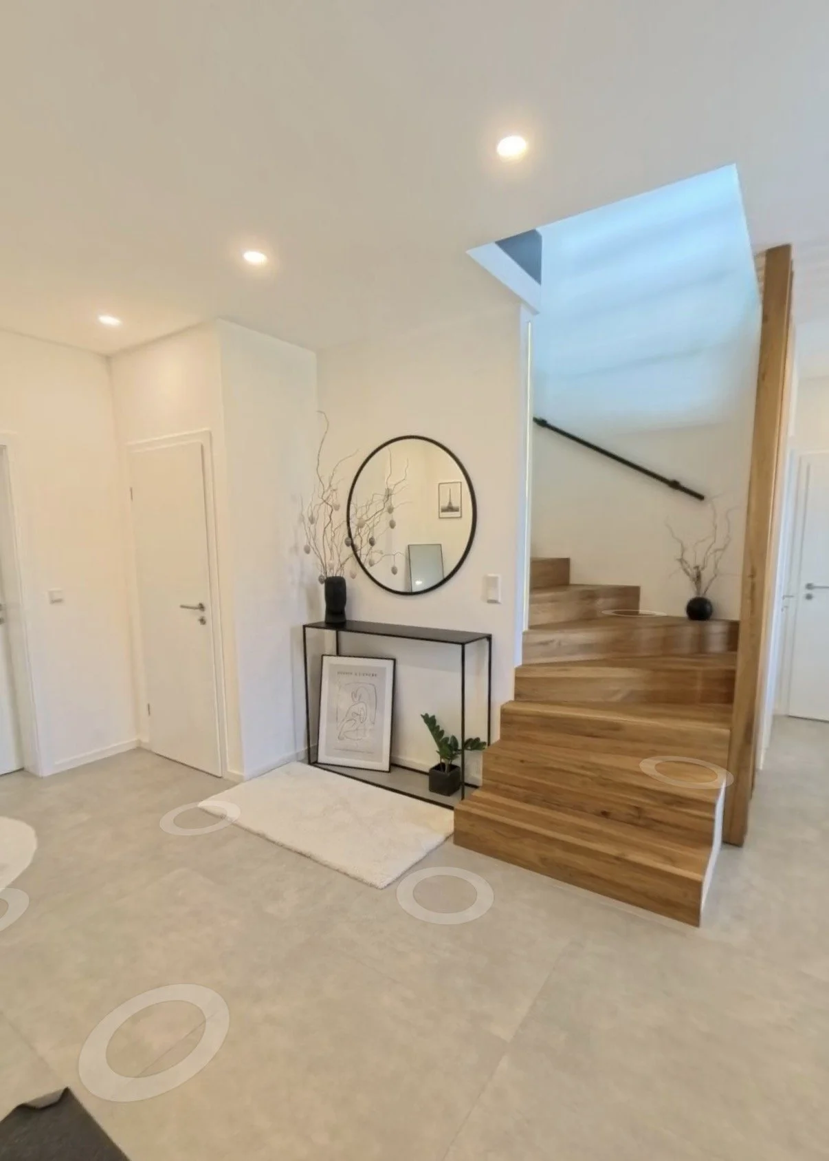 Ein moderner Eingangsbereich mit weißer Wand, Holzstufen, einem schwarzen Spiegel und Dekorationen wie Pflanzen und Bilder.