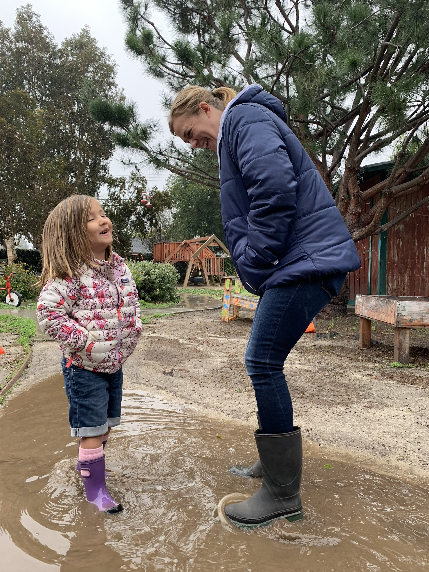 Smiling teacher jumping in puddles with a happy child at an outdoor preschool