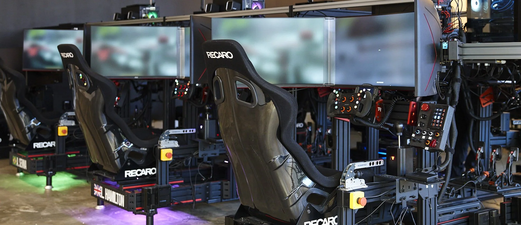 Person using a racing simulator with multiple monitors and a steering wheel controller.