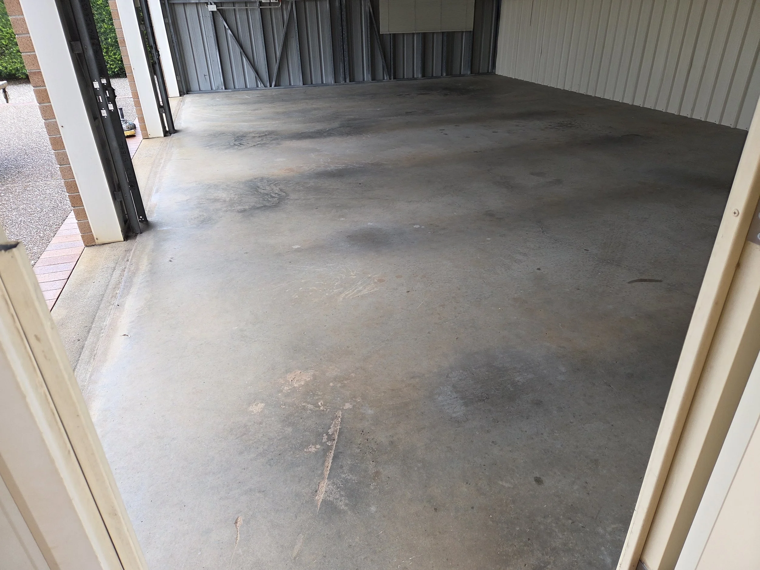 Empty garage with a concrete floor, partially open garage door, and metal walls.