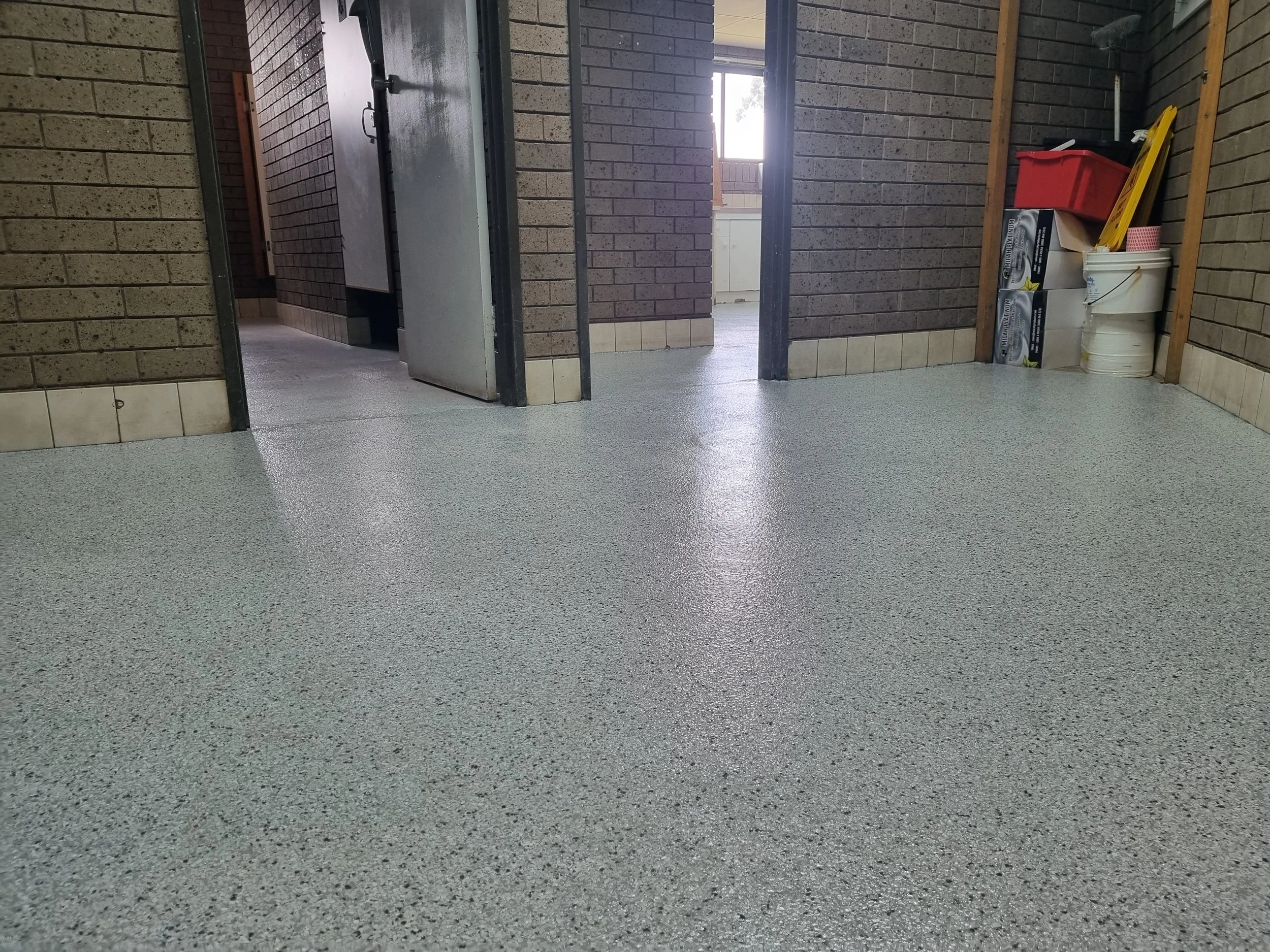 Indoor room with speckled gray epoxy flooring, brick walls, and open doors leading outside to a balcony or patio.