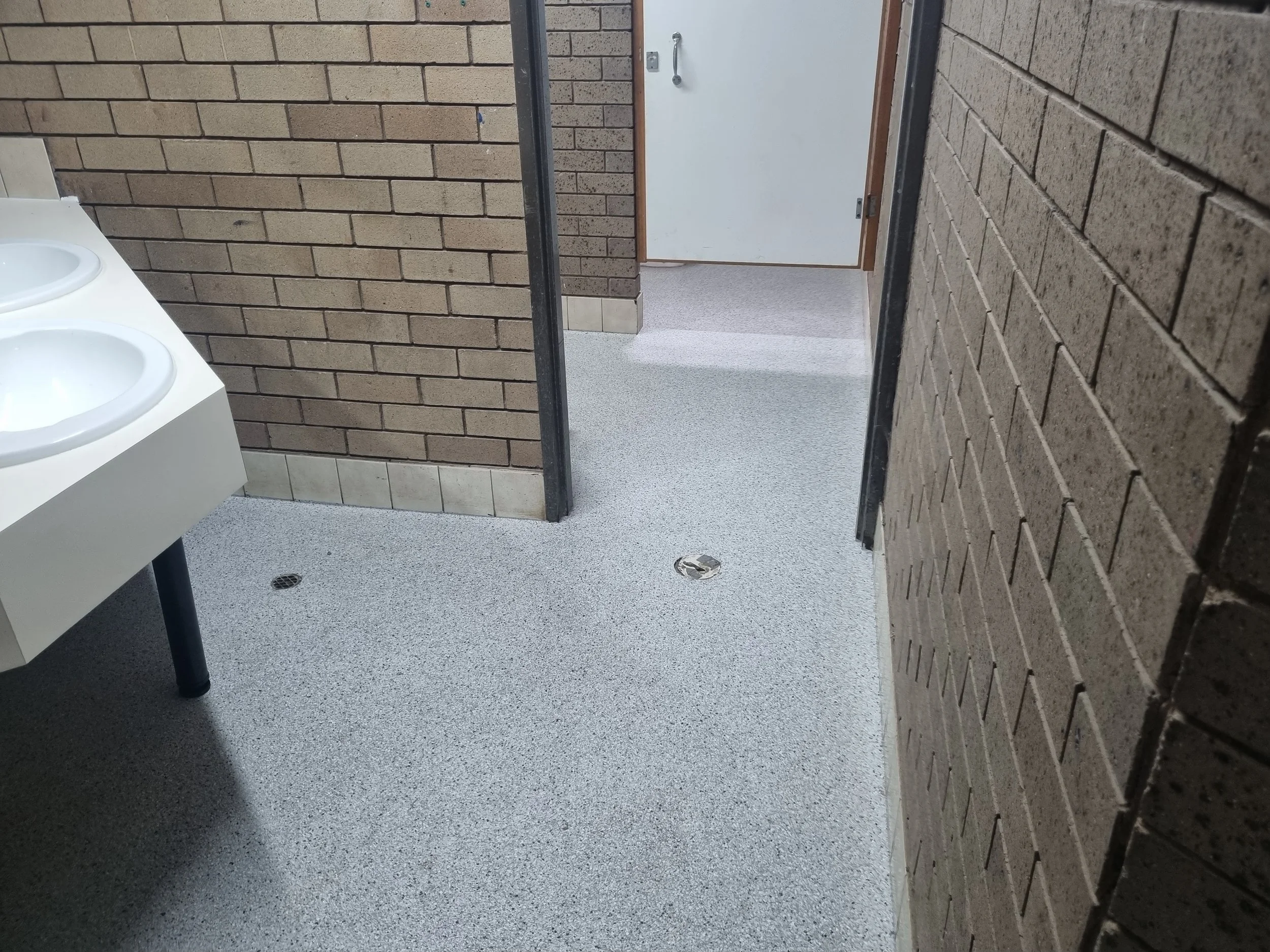 Public restroom with brick walls, a double-sink vanity, and an open door leading to a hallway.