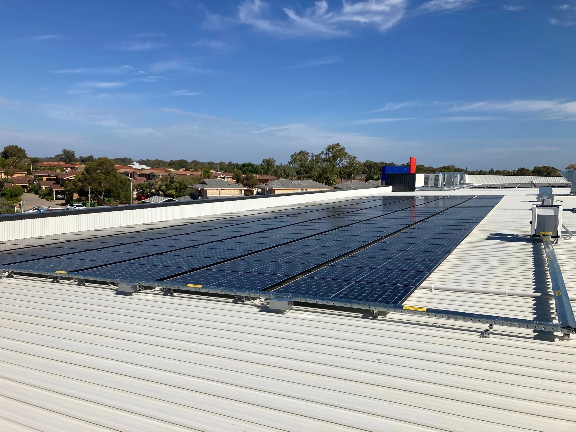 Solar panels installed on a white roof, with a suburban neighborhood and blue sky in the background.