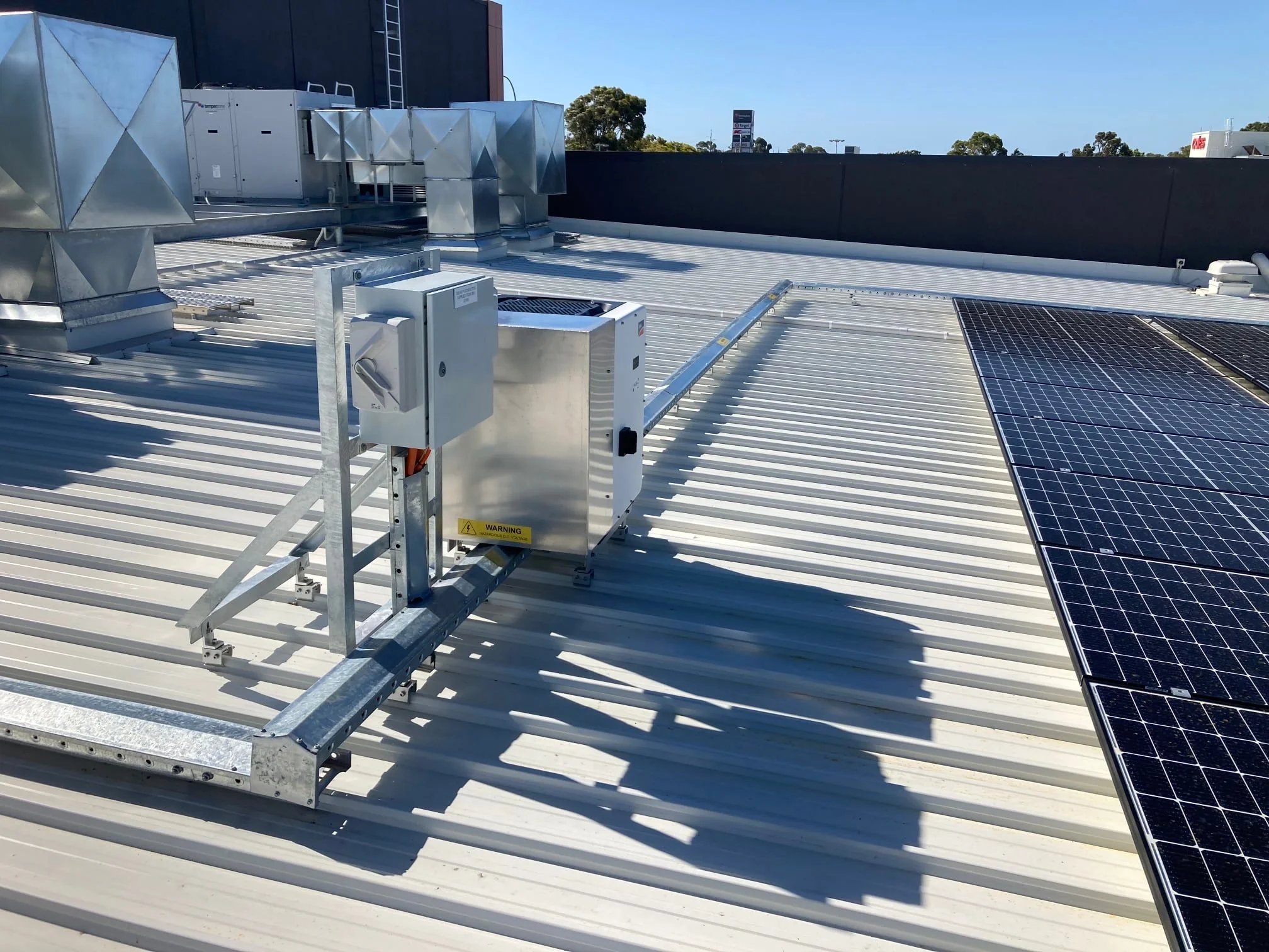 Rooftop view showing solar panels, HVAC units, and electrical equipment on a metal roof under clear blue sky.