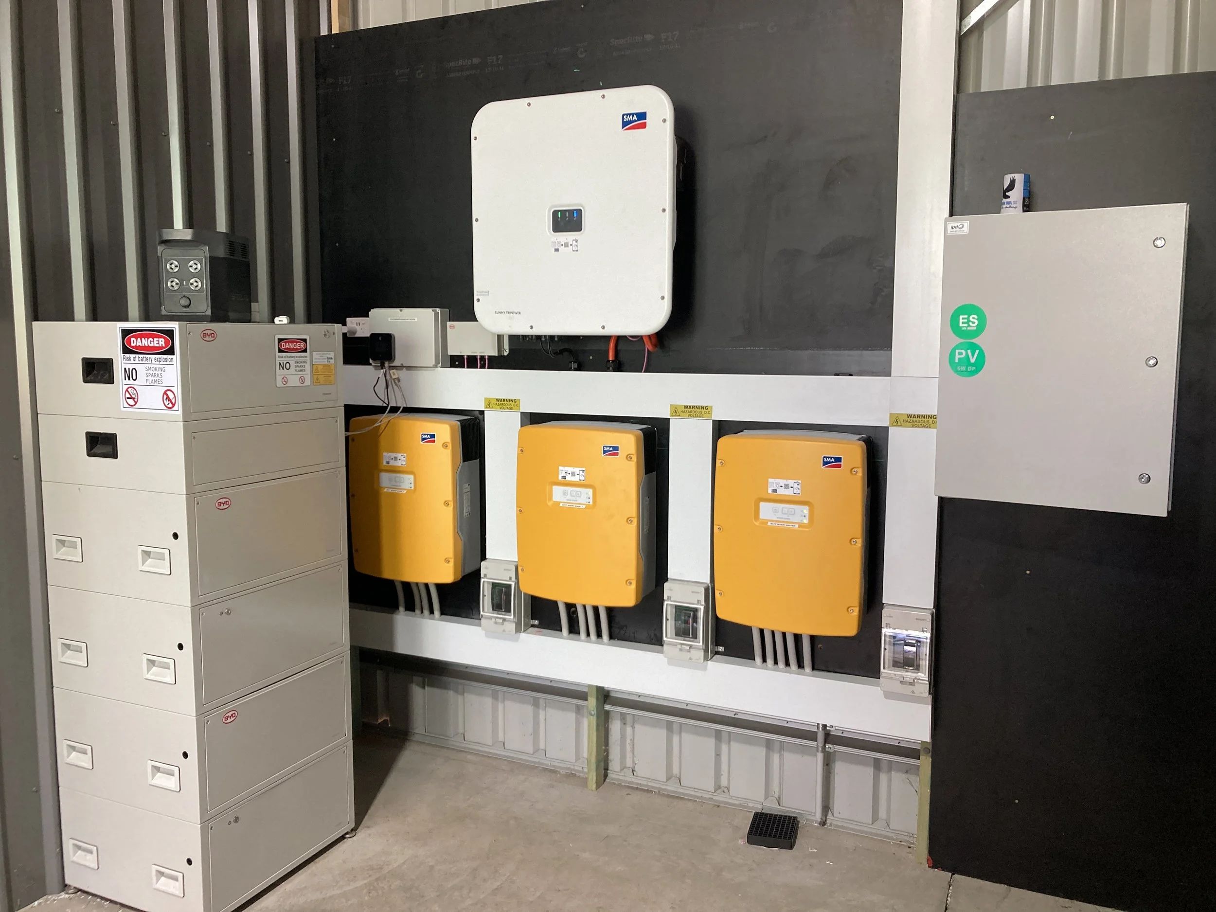 Electric vehicle charging station with three orange chargers, electrical boxes, and safety warning labels