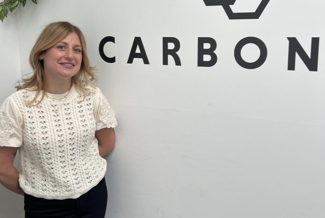Woman standing in front of a white wall with the word 'CARBON' written on it and a geometric logo above.