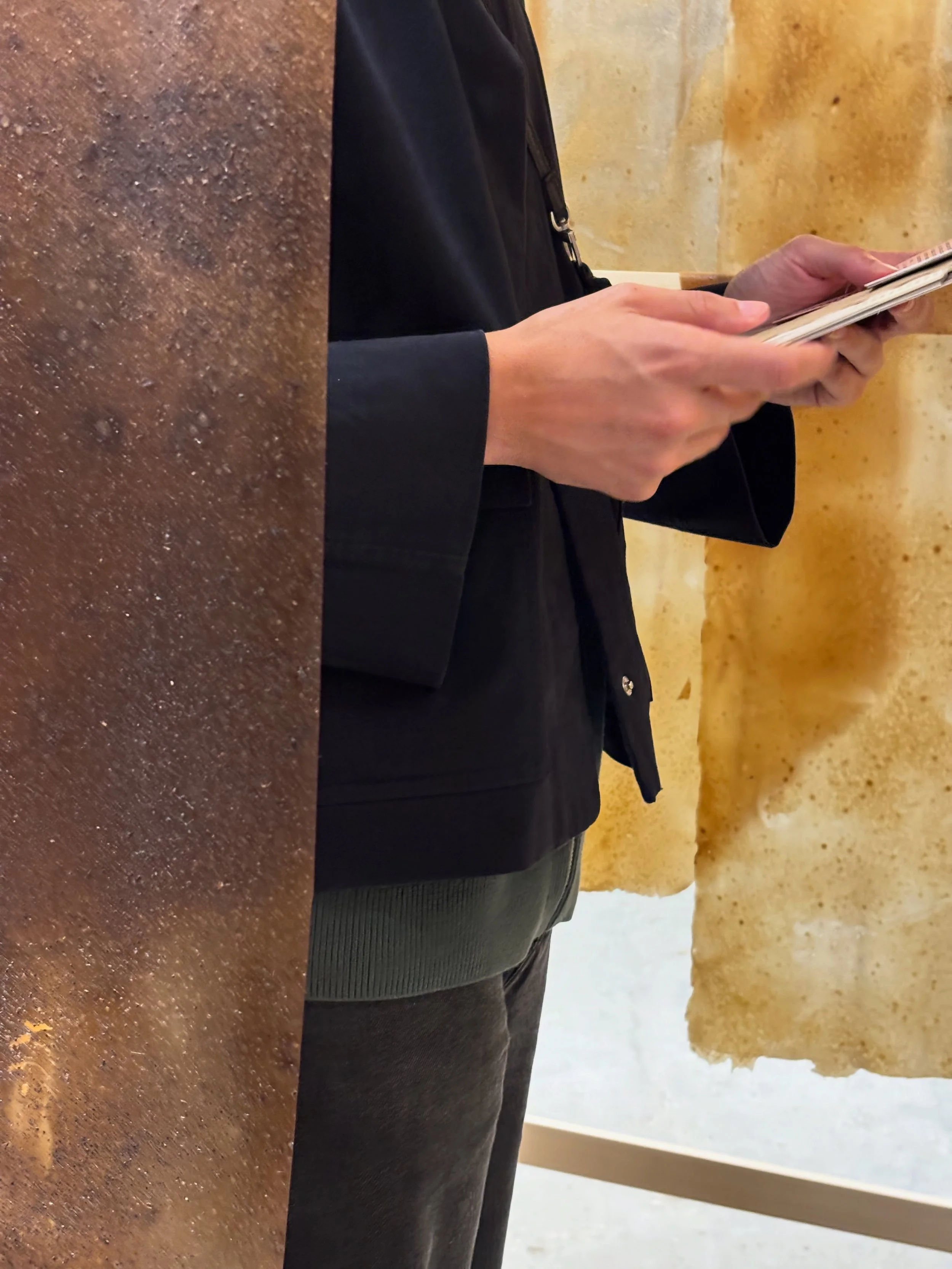 Persona che legge un menu o un dispositivo digitale in un ambiente interno, con indumenti scuri e un tavolo di legno.