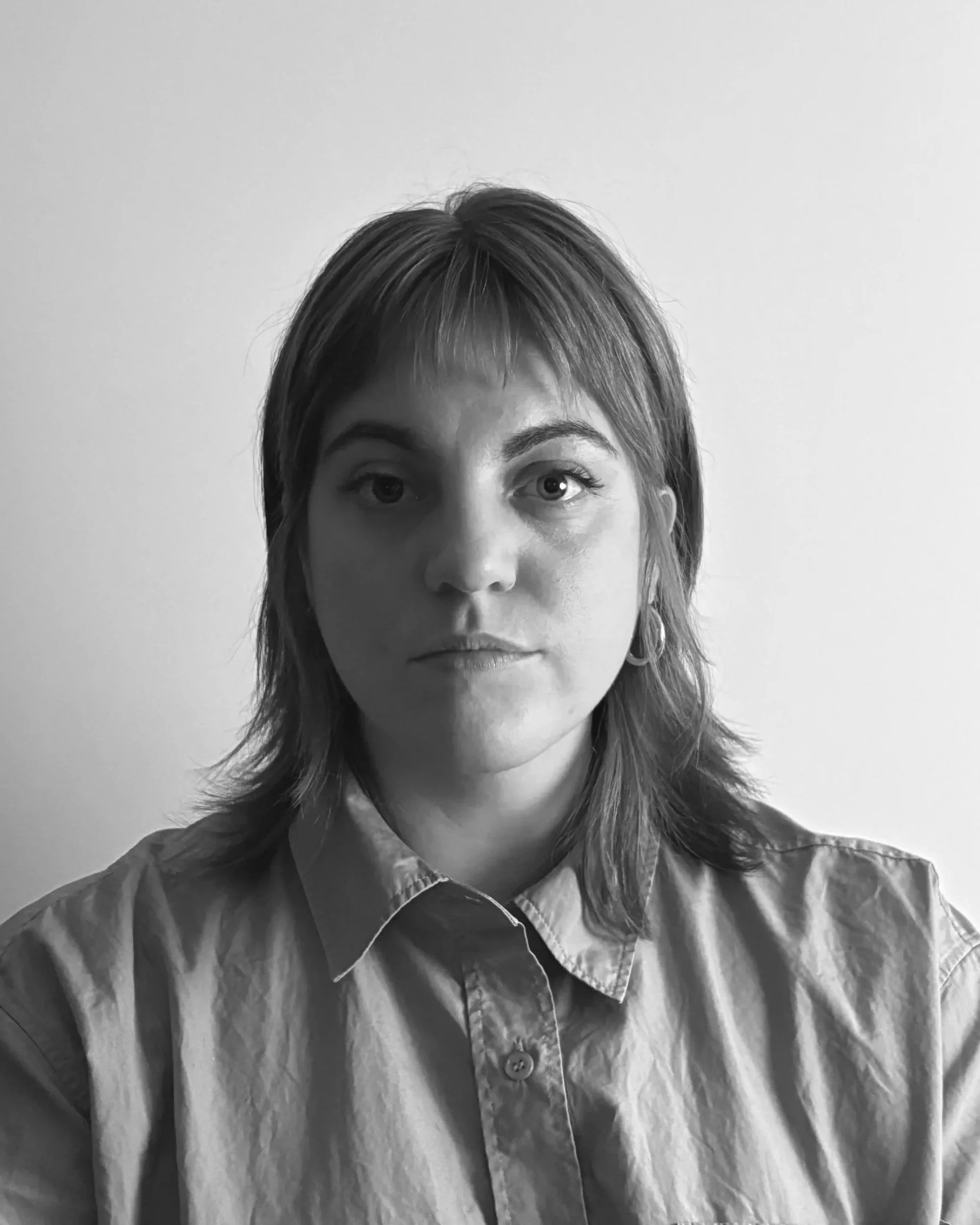 Ritratto in bianco e nero di una donna con capelli corti e occhi chiari, indossa una camicia con colletto, sfondo chiaro e semplice.