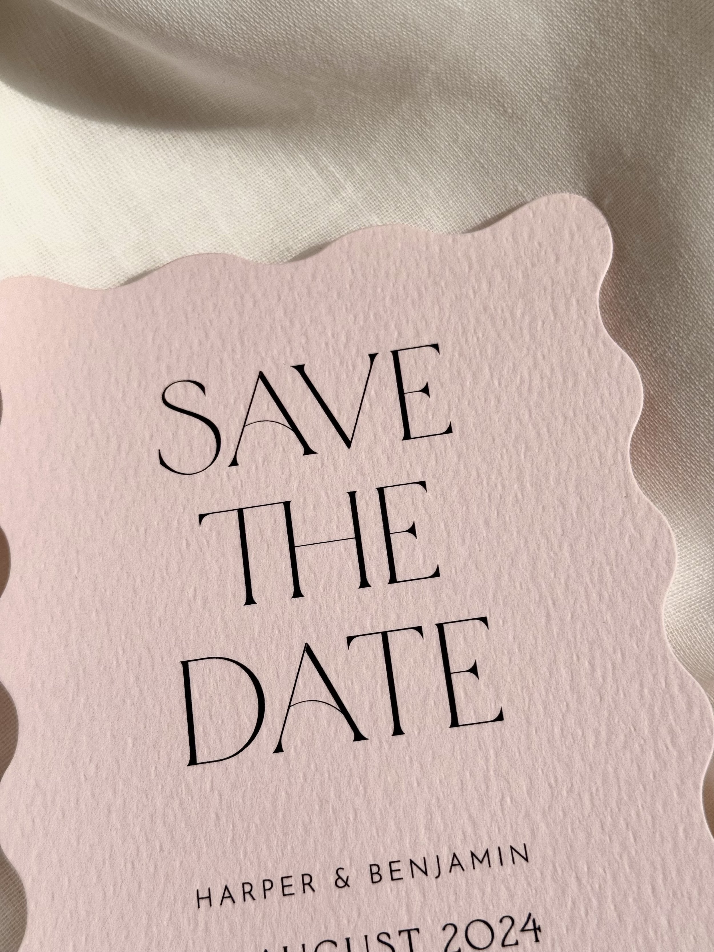 A pink textured card with scalloped edges reading 'Save the Date' for Harper and Benjamin's wedding in August 2024.