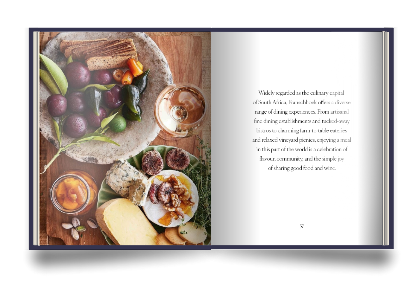 The Franschhoek Experience Book with an image of a cheese board with grapes, fruit, bread, and wine at Bischendal estate on the left page, and a paragraph describing South African cuisine on the right page.