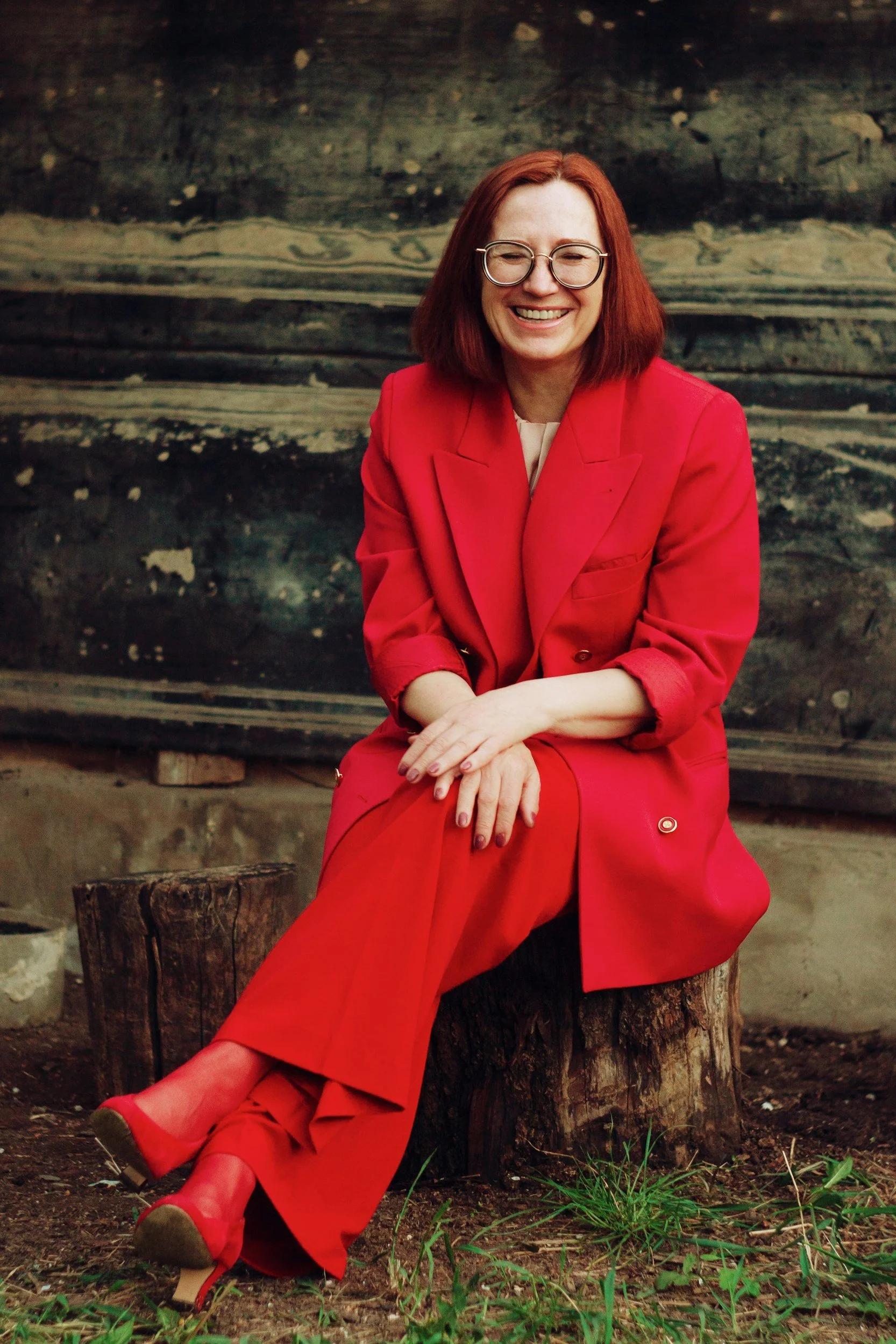 a mature woman with dyed red hair wears a bright red suit looking happy