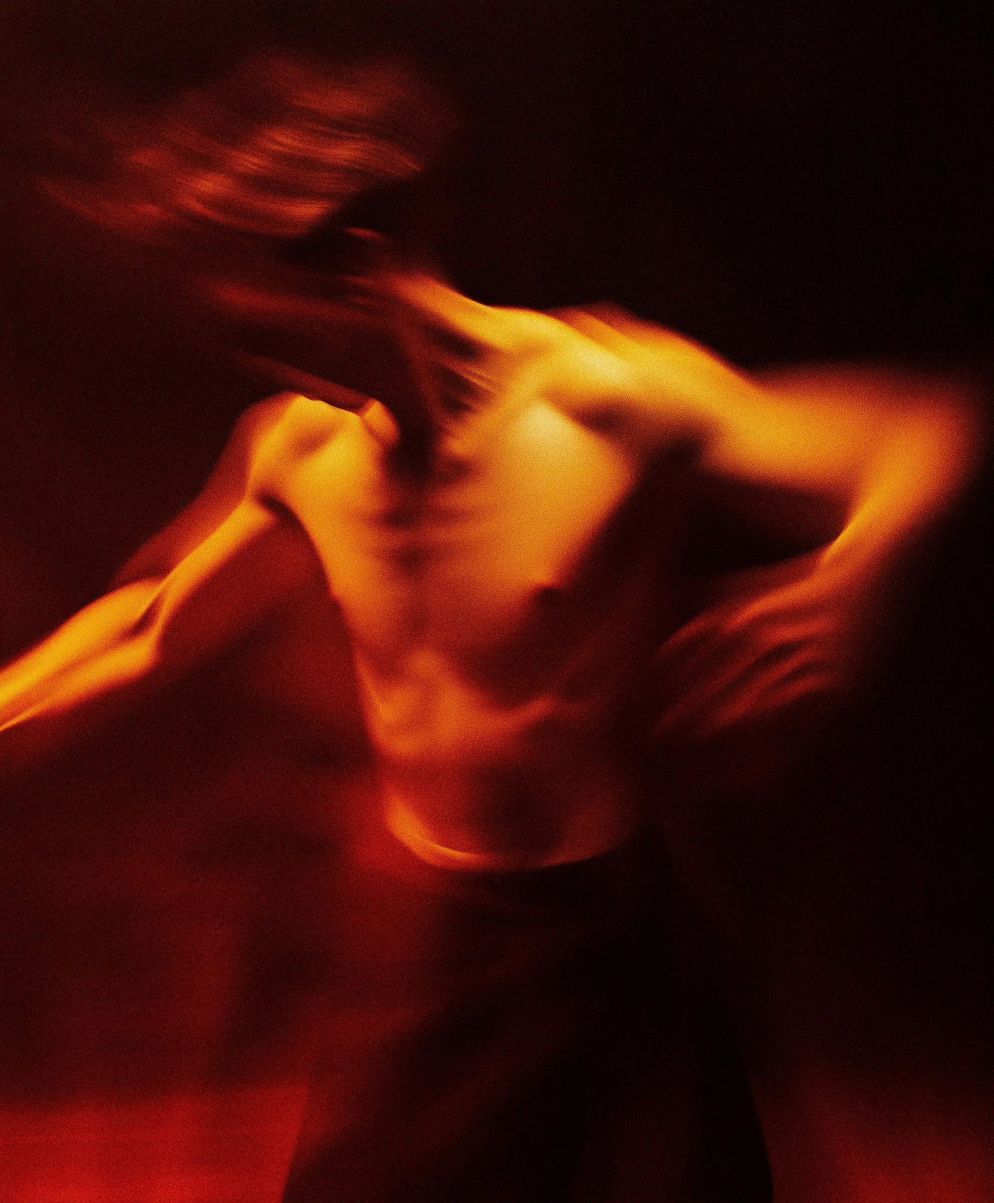Blurred image of a nude person with long hair, posing against a dark background with red-orange lighting.