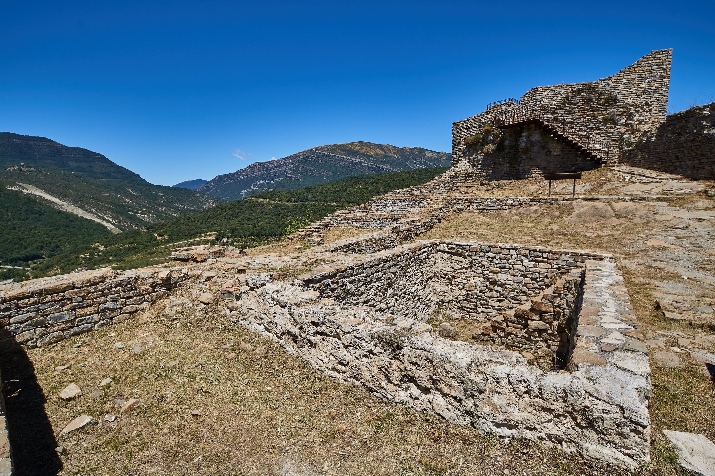 Ruinas antiguas de piedra en una montaña, cielo azul despejado.