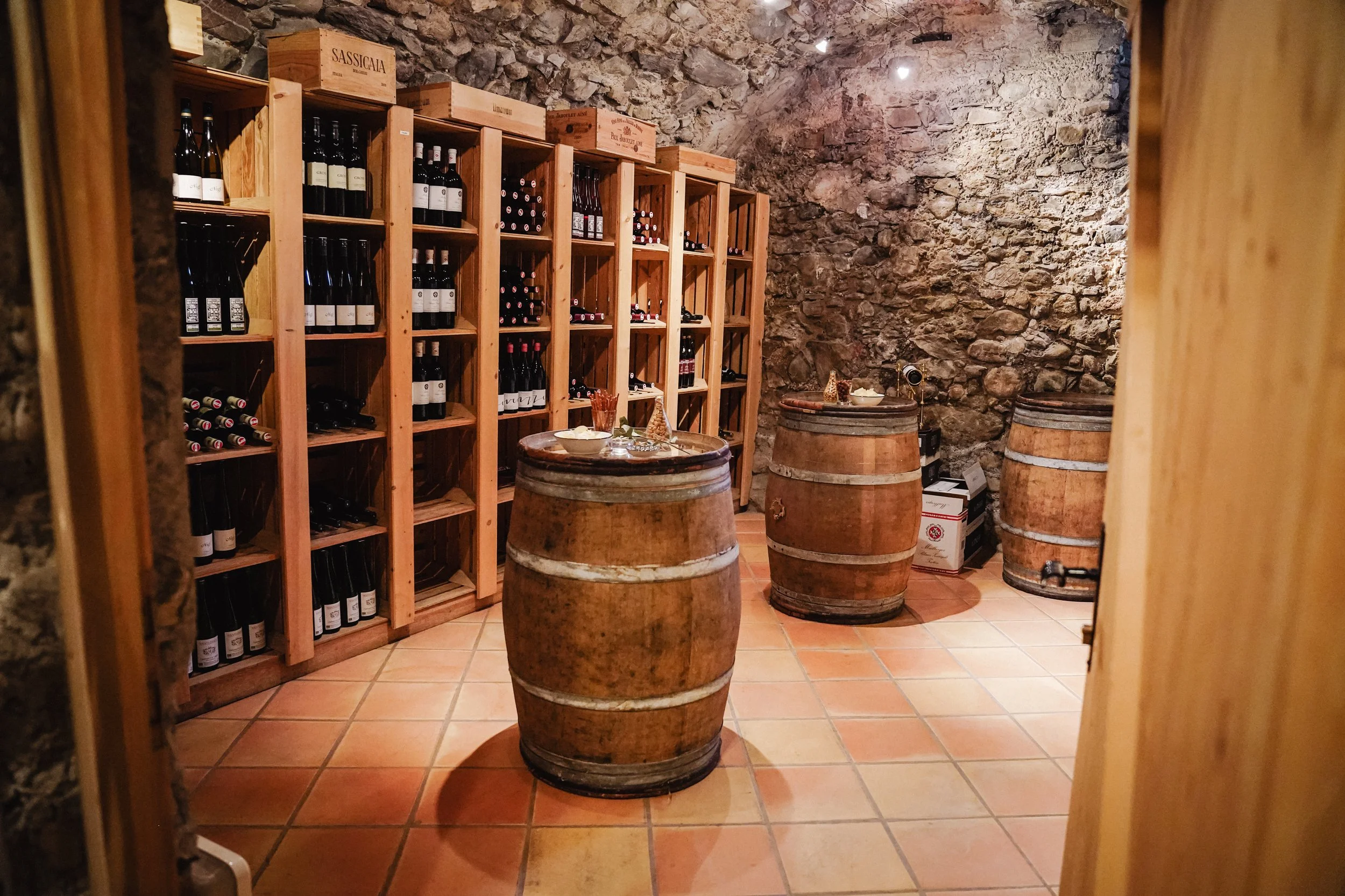Eine Weinkellerei mit Weinregalen, alten Weinfässern und Flaschen an der Wand.