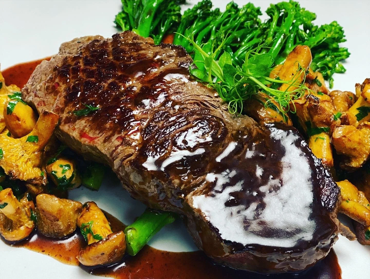 Ein geröstetes Stück Rindfleisch mit brauner Sauce, umgeben von sautierten Champignons, Kartoffelwürfeln und grünem Gemüse, garniert mit frischen Kräutern