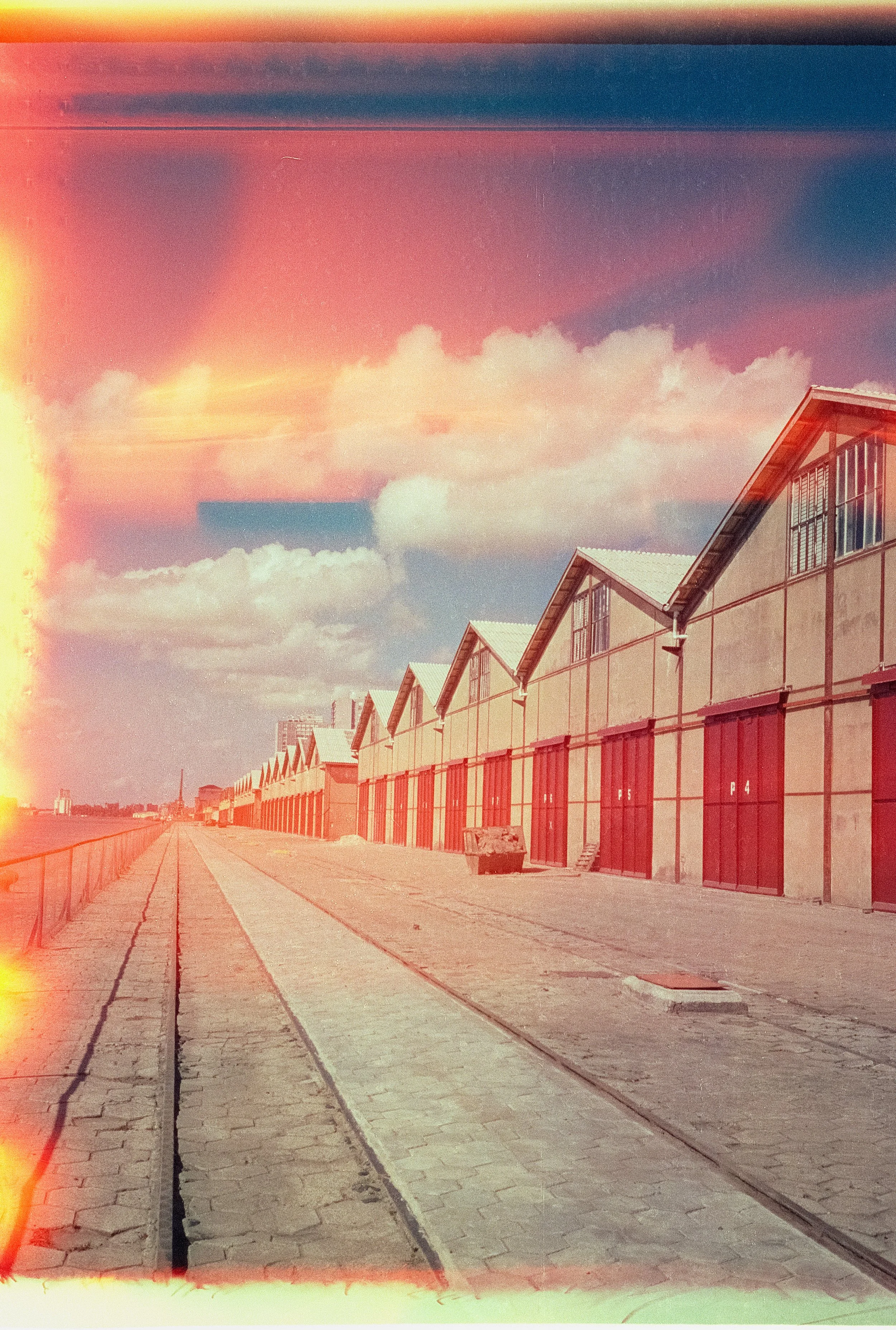 Rows of modern townhouses with large windows, set along a paved path, under a colorful sunset sky with scattered clouds.