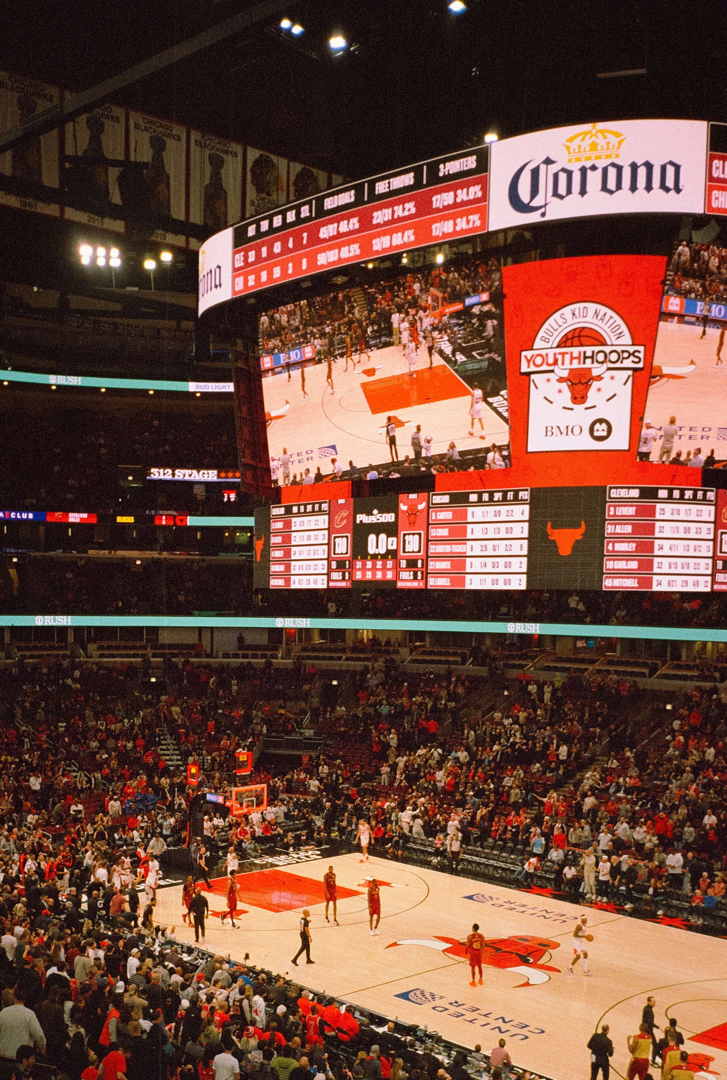 An NBA basketball game with players on the court and spectators in the stands, viewed from the seating area near the basket.