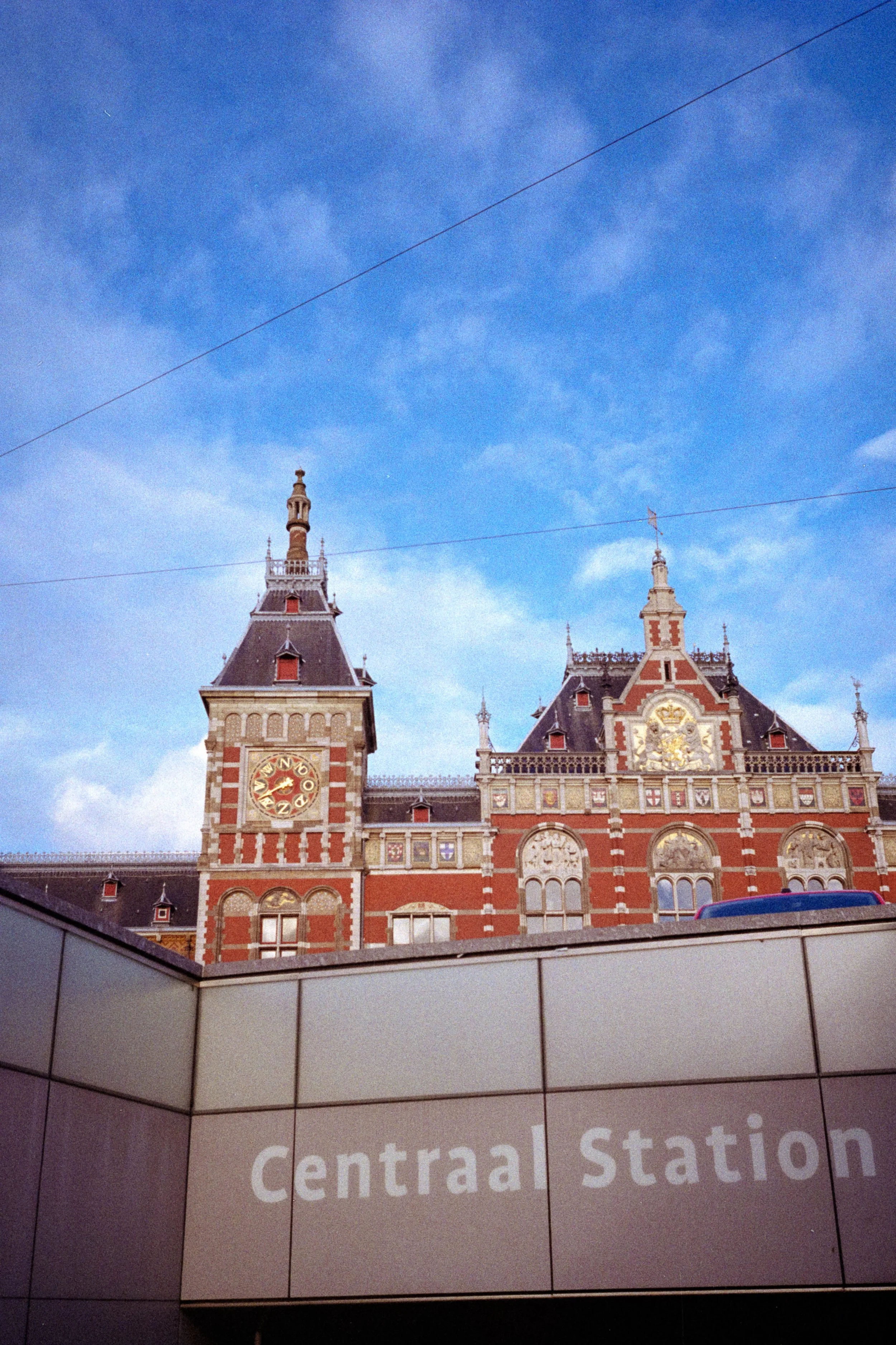 Photograph of a building with a clock tower and ornate architecture, likely part of a historical train station, against a blue sky with scattered clouds. The image is partially obscured by a sign that reads 'central station'.