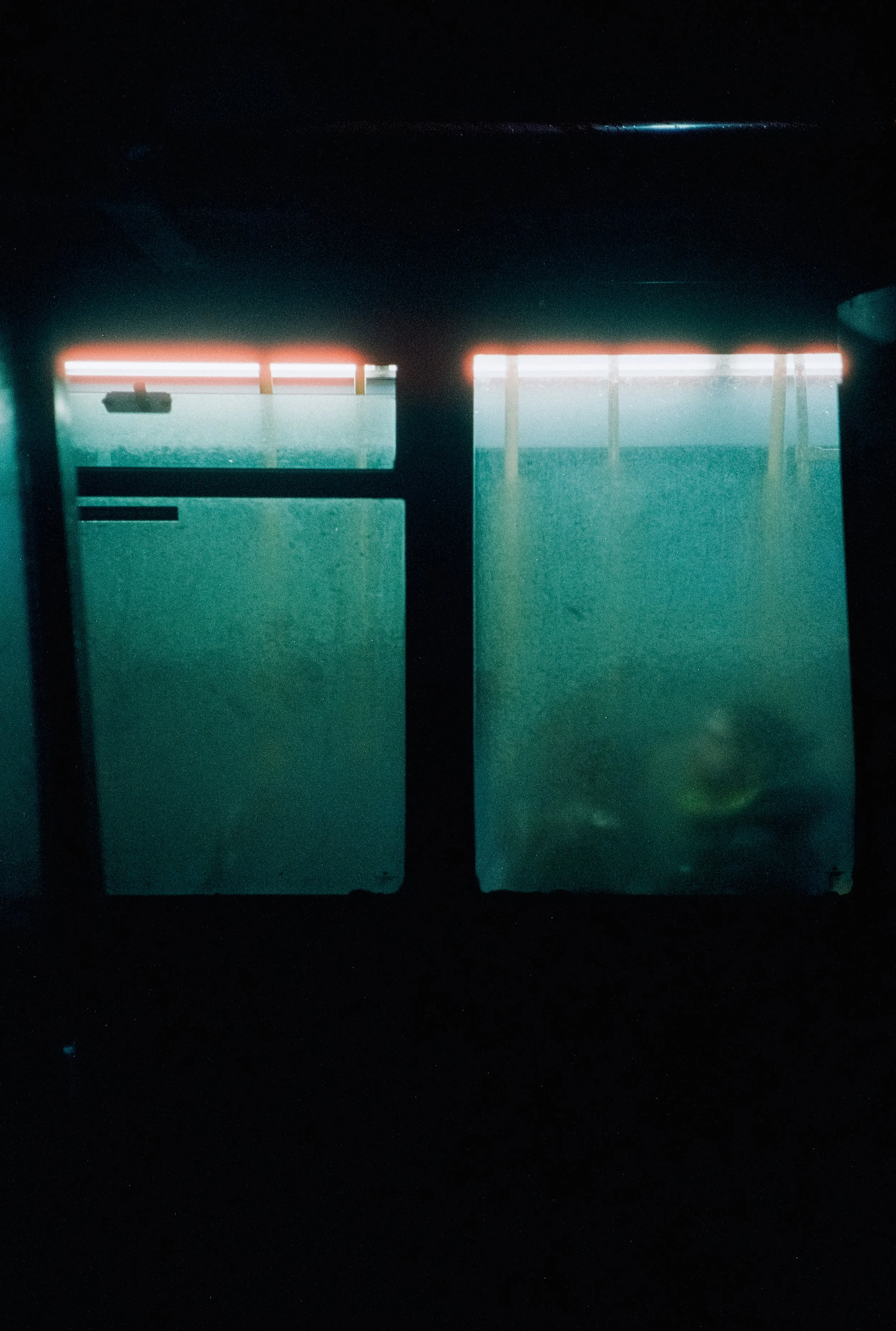 A dark scene viewed through a window with curtains, showing a foggy or misty landscape outside with some faint lights and structures in the distance.
