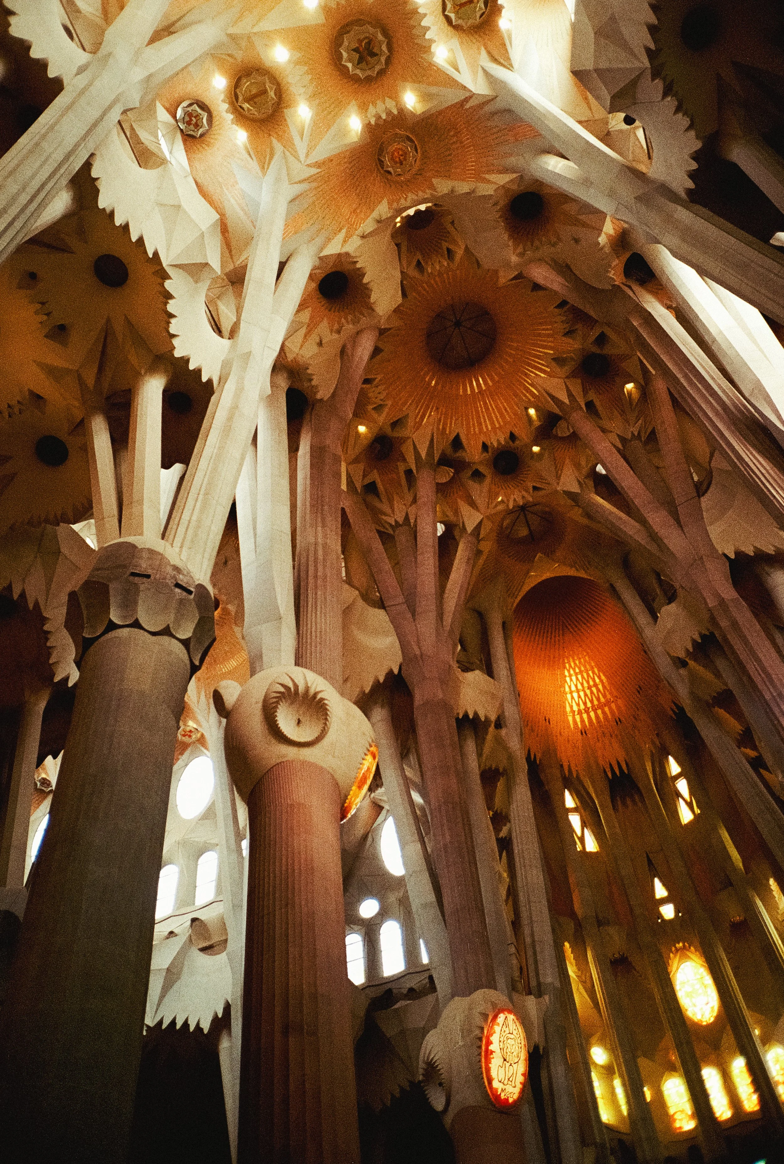 Interior of a church with intricate wooden ceiling designs, columns, and stained glass windows, illuminated by warm lighting.