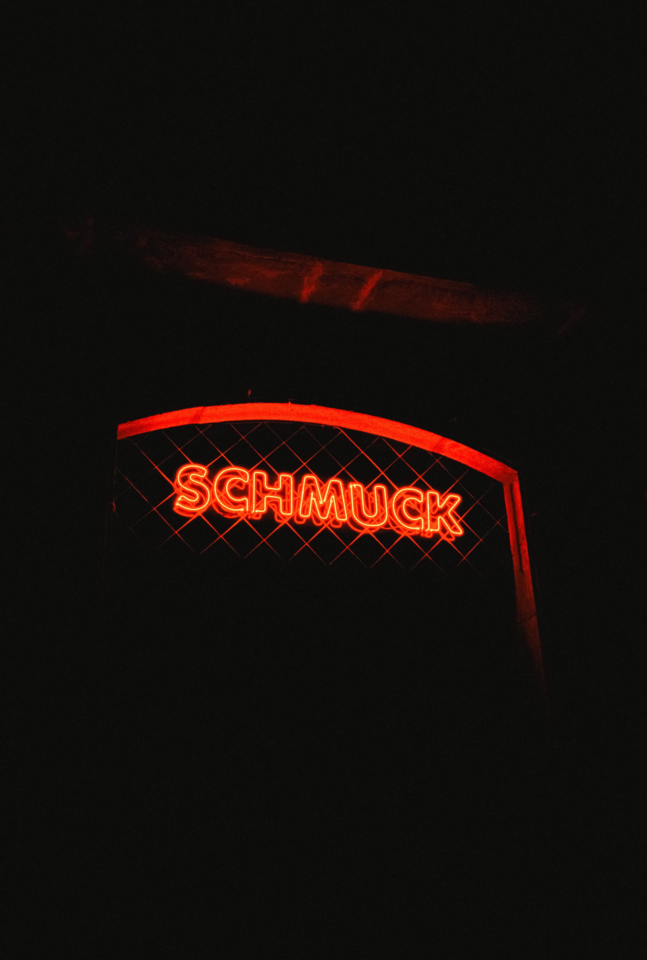 Red neon sign spelling 'SCHMUCK' against dark background.