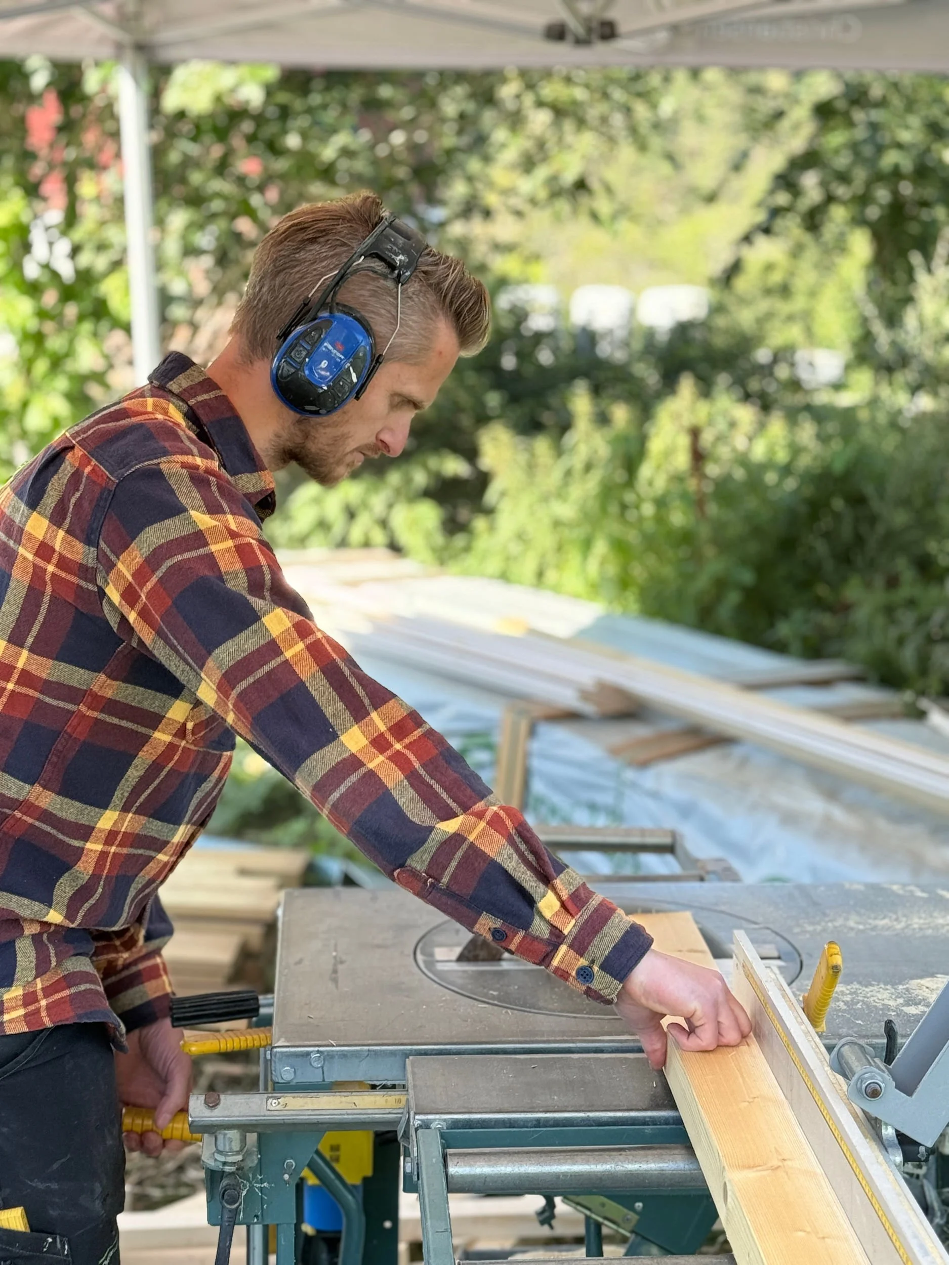 Person som bruker øreklokker og skjorte, som skjærer tre med en sirkelsag utendørs.