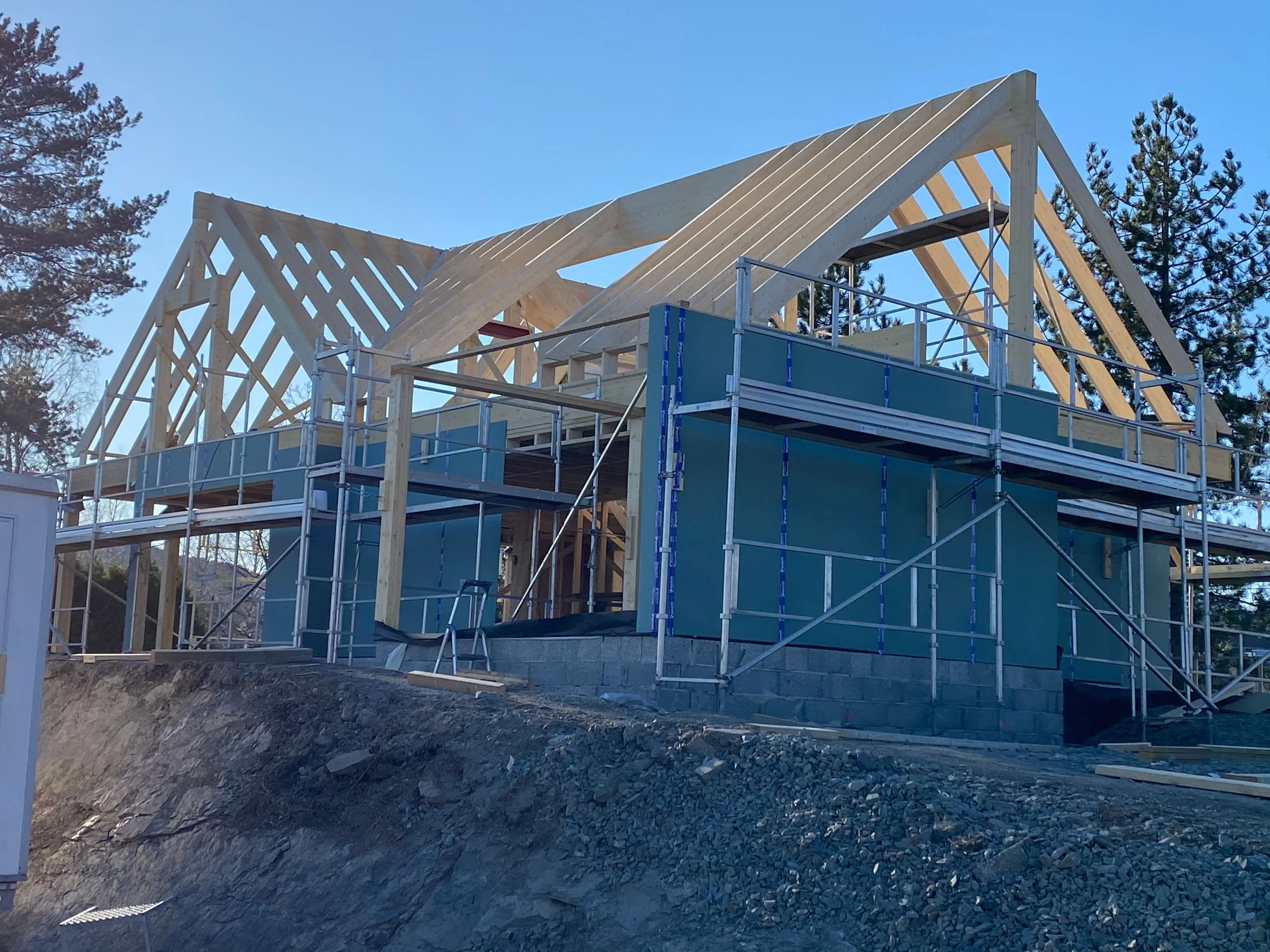 Verkset rammer til bygging av hus på byggetomt, med trær i bakgrunnen og en klar blå himmel.