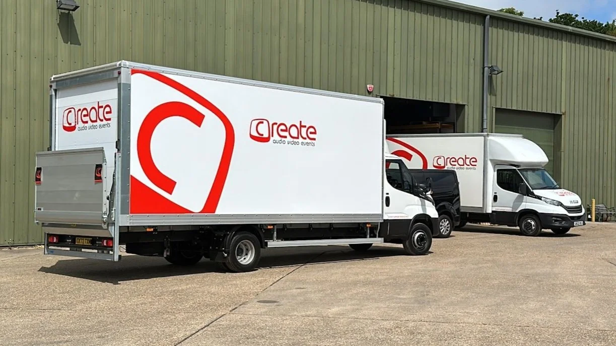 Three white delivery trucks with 'Create Audio Video Events' logo parked outside a large green industrial building.