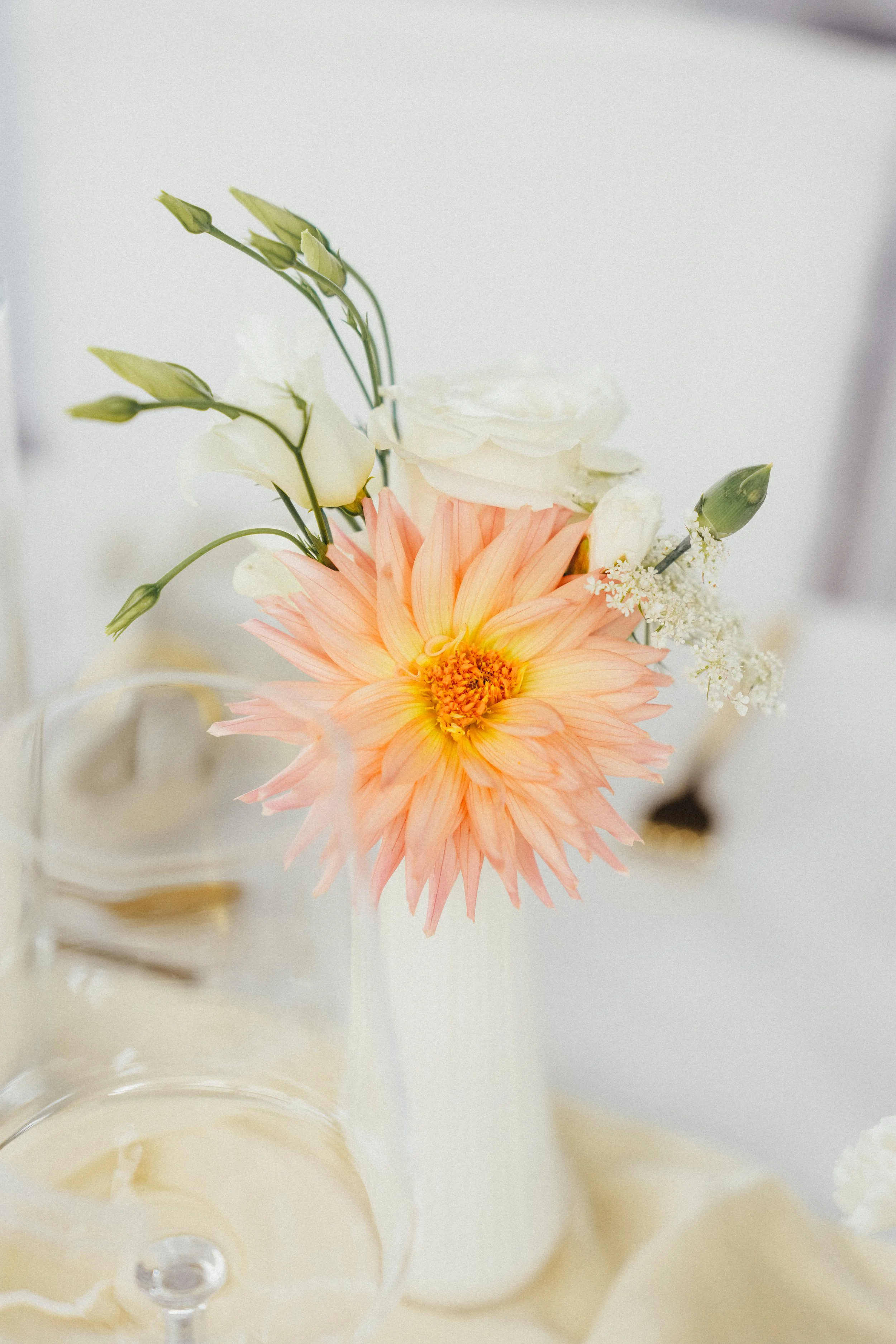 Blumenvase mit peachfarbener Dahlie und weißen Blumen auf einem Tisch.