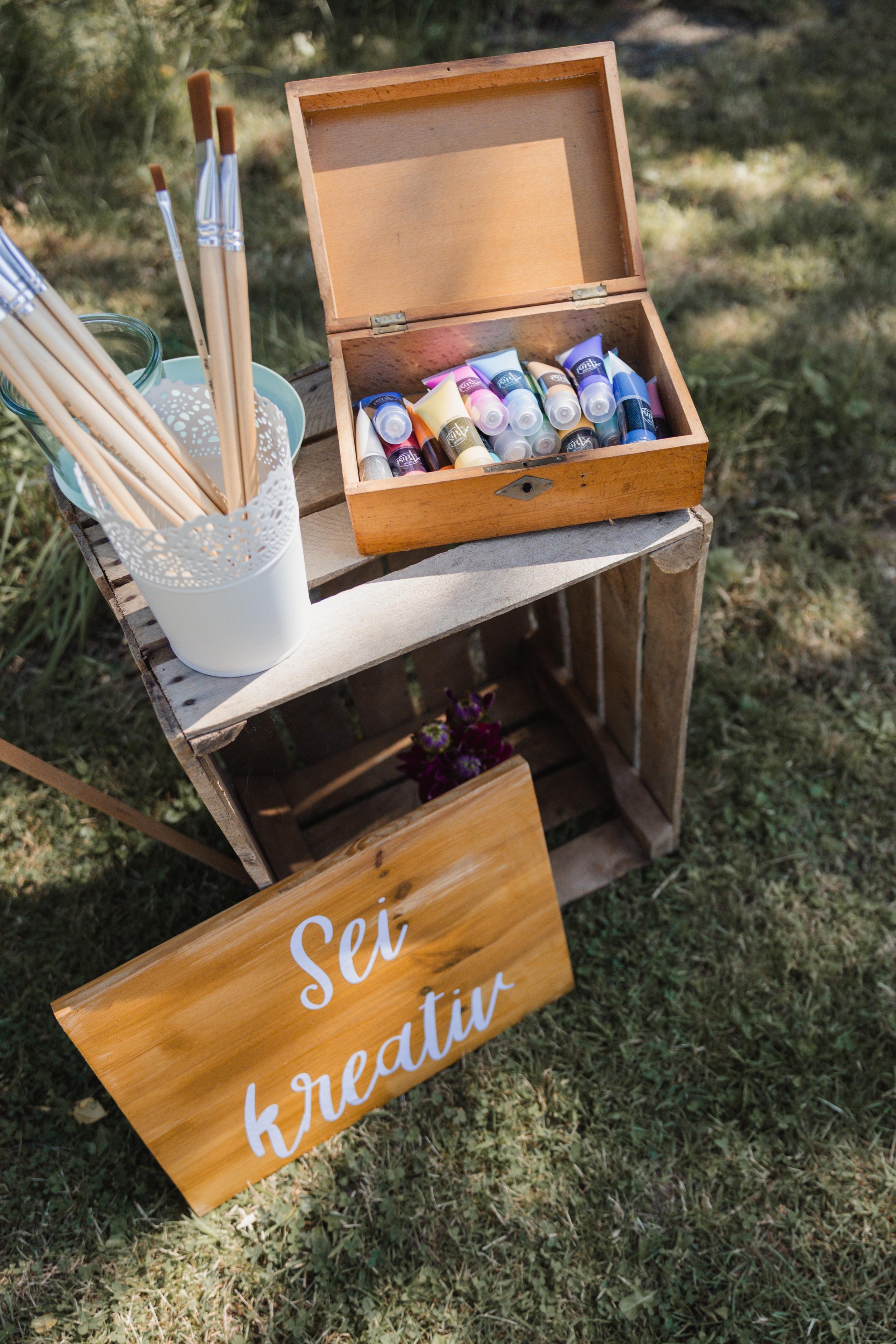 Ein Holztablett mit Malfarben, Pinsel und einem Schild mit der Aufschrift 'Sei kreativ'.