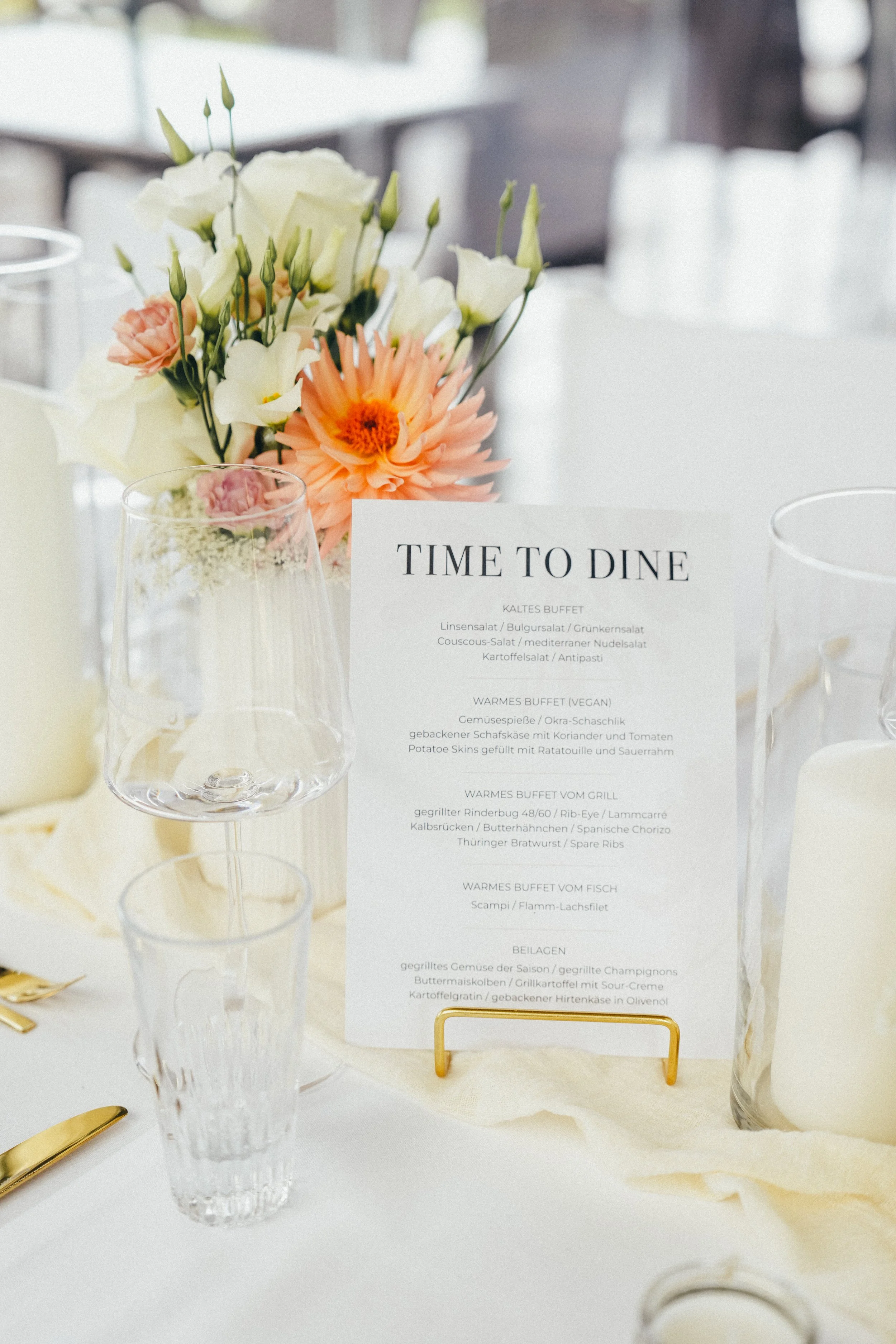 Esstisch mit Blumenstrauß, Weingläsern und Menükarte auf einer Hochzeits- oder Festtafel. Alt-Text: Tischdekoration Hochzeit Kiel mit goldenen Kerzenständern