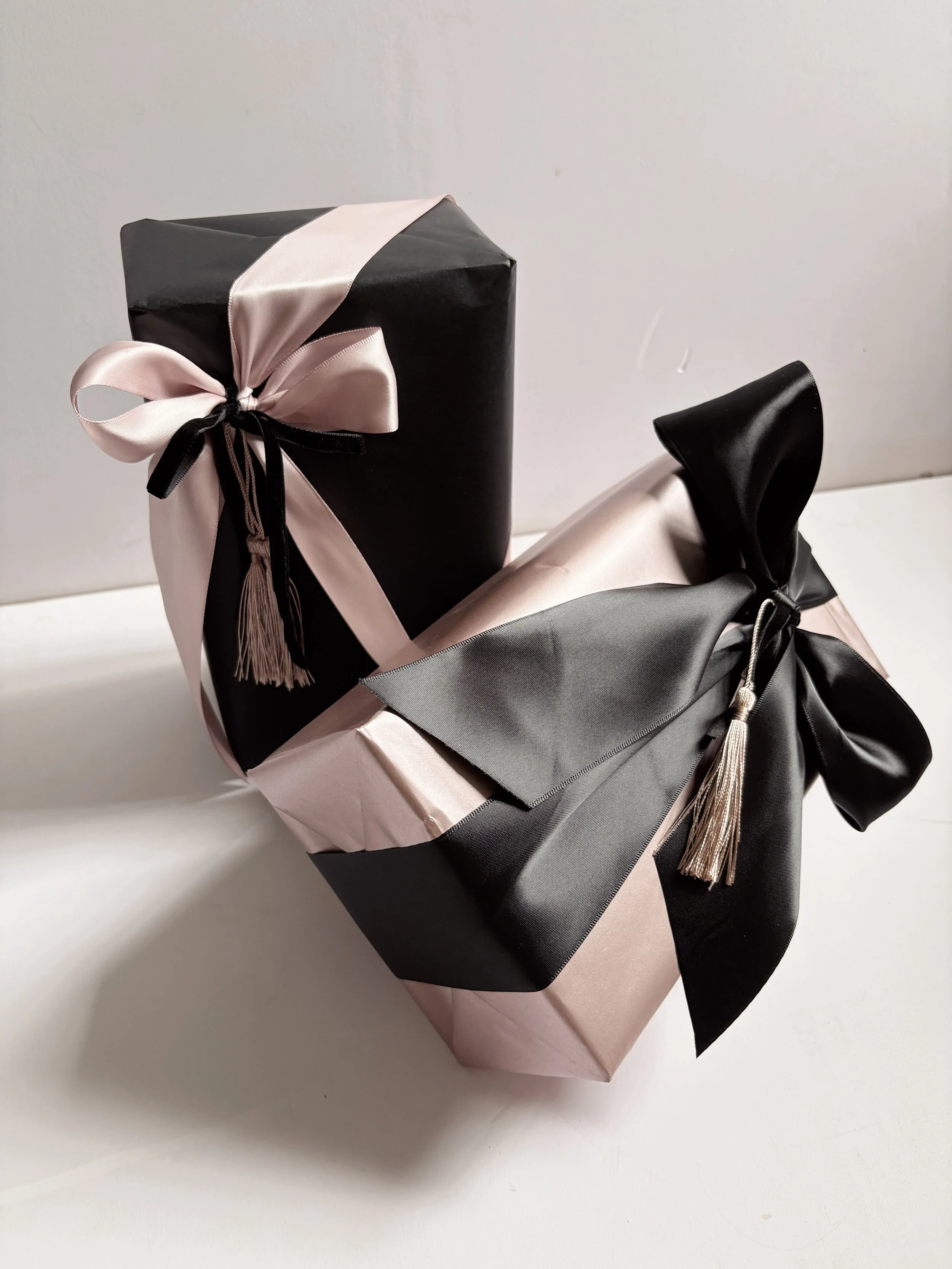 Two wrapped gift boxes with black and pink wrapping paper, decorated with pink and black satin ribbons and tassels | Luxury Gift Wrapping & Custom Hampers