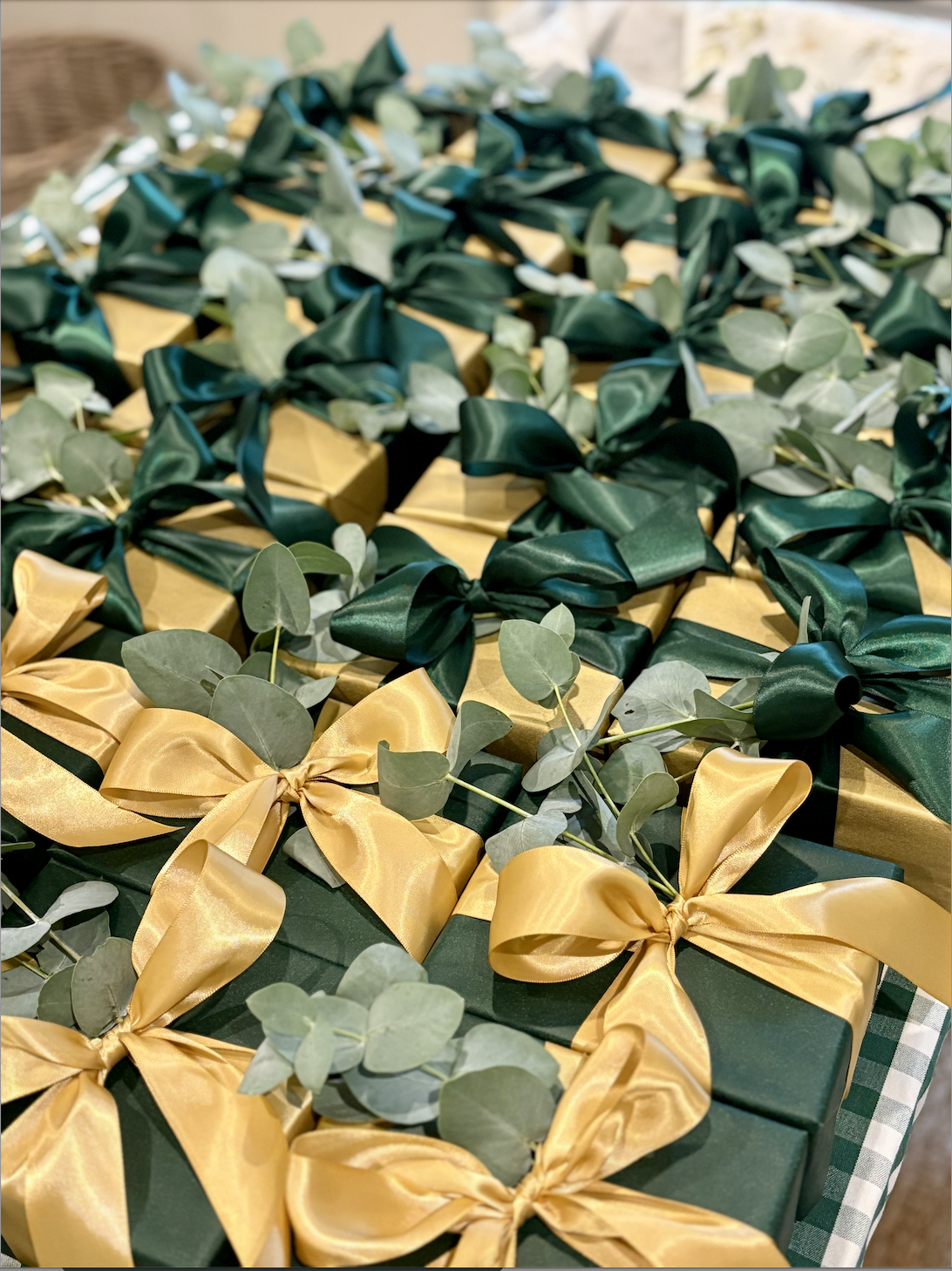 A table filled with gift boxes wrapped in green paper, decorated with gold ribbons and green foliage | Luxury Gift Wrapping & Custom Hampers