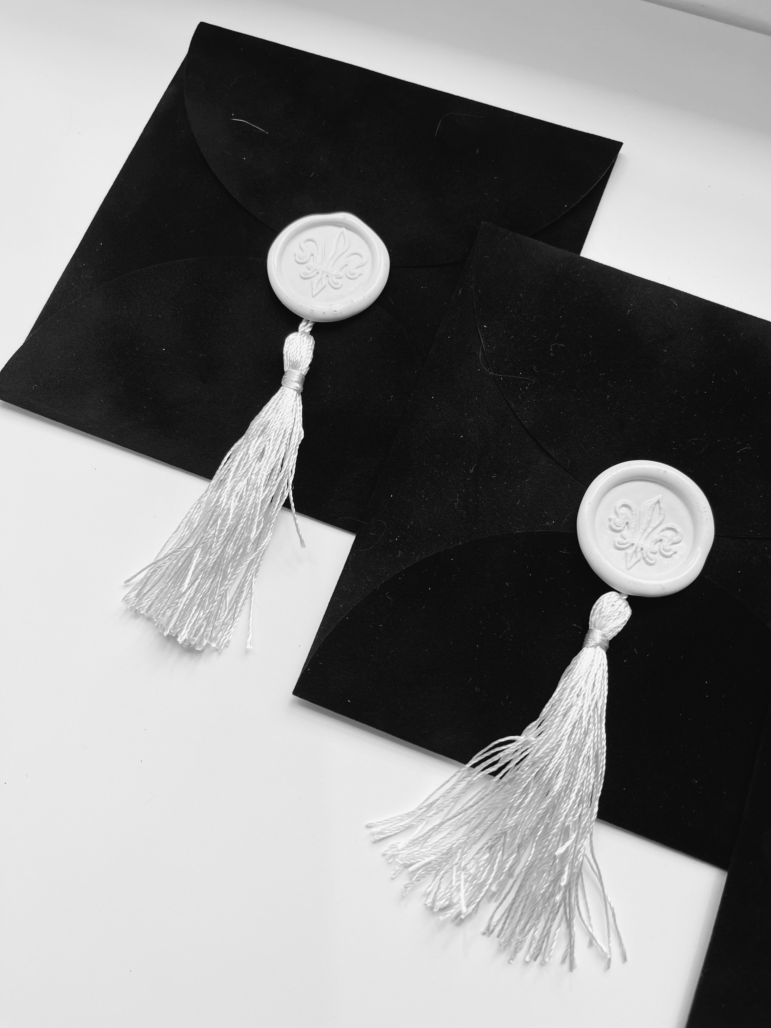Two black envelopes with white wax seals stamped with a fleur-de-lis design and white tassels | Luxury Gift Wrapping & Custom Hampers.