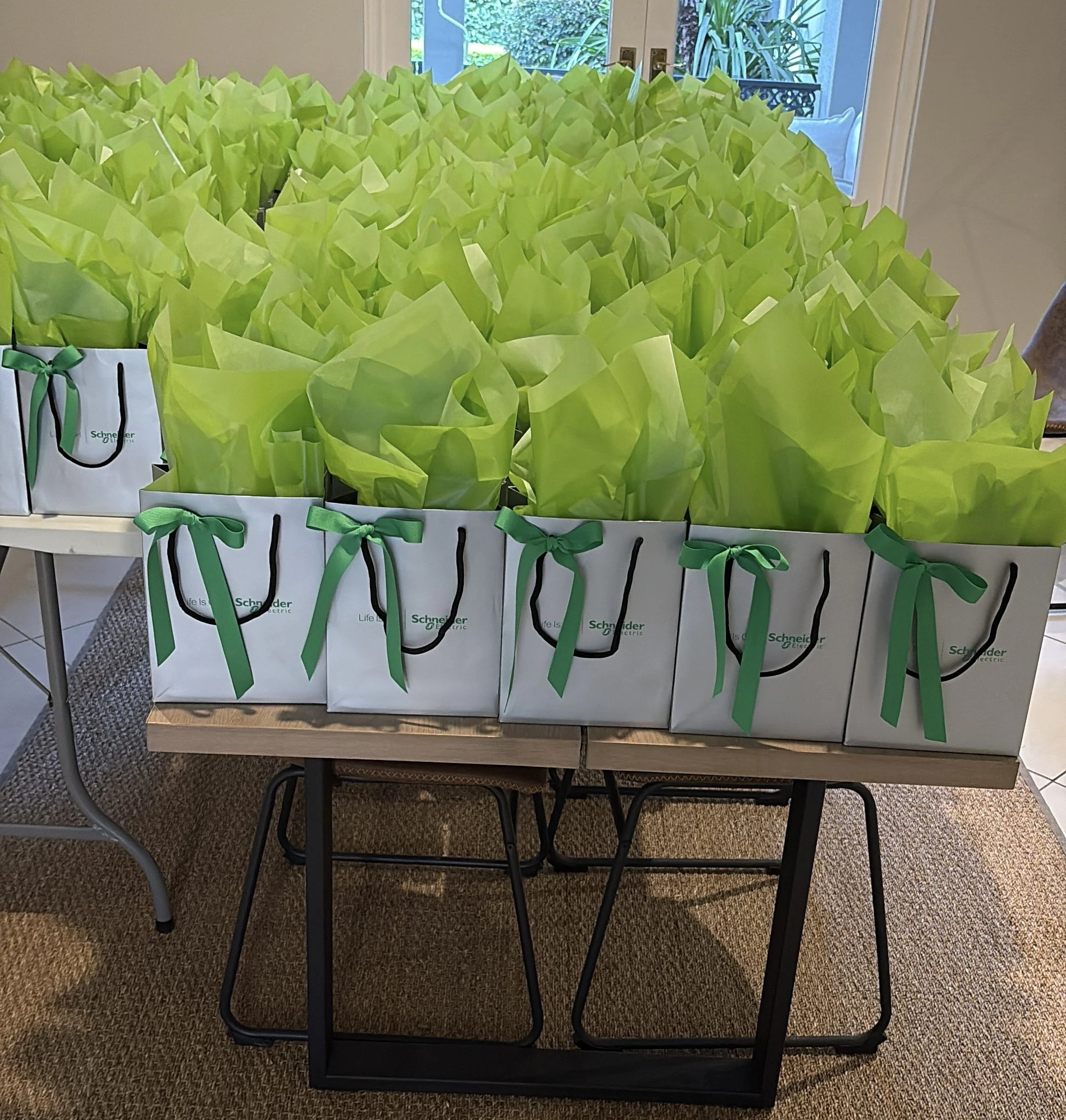 Multiple white gift bags with green ribbon bows, filled with green tissue paper, arranged on a table indoors | Luxury Gift Wrapping & Custom Hampers