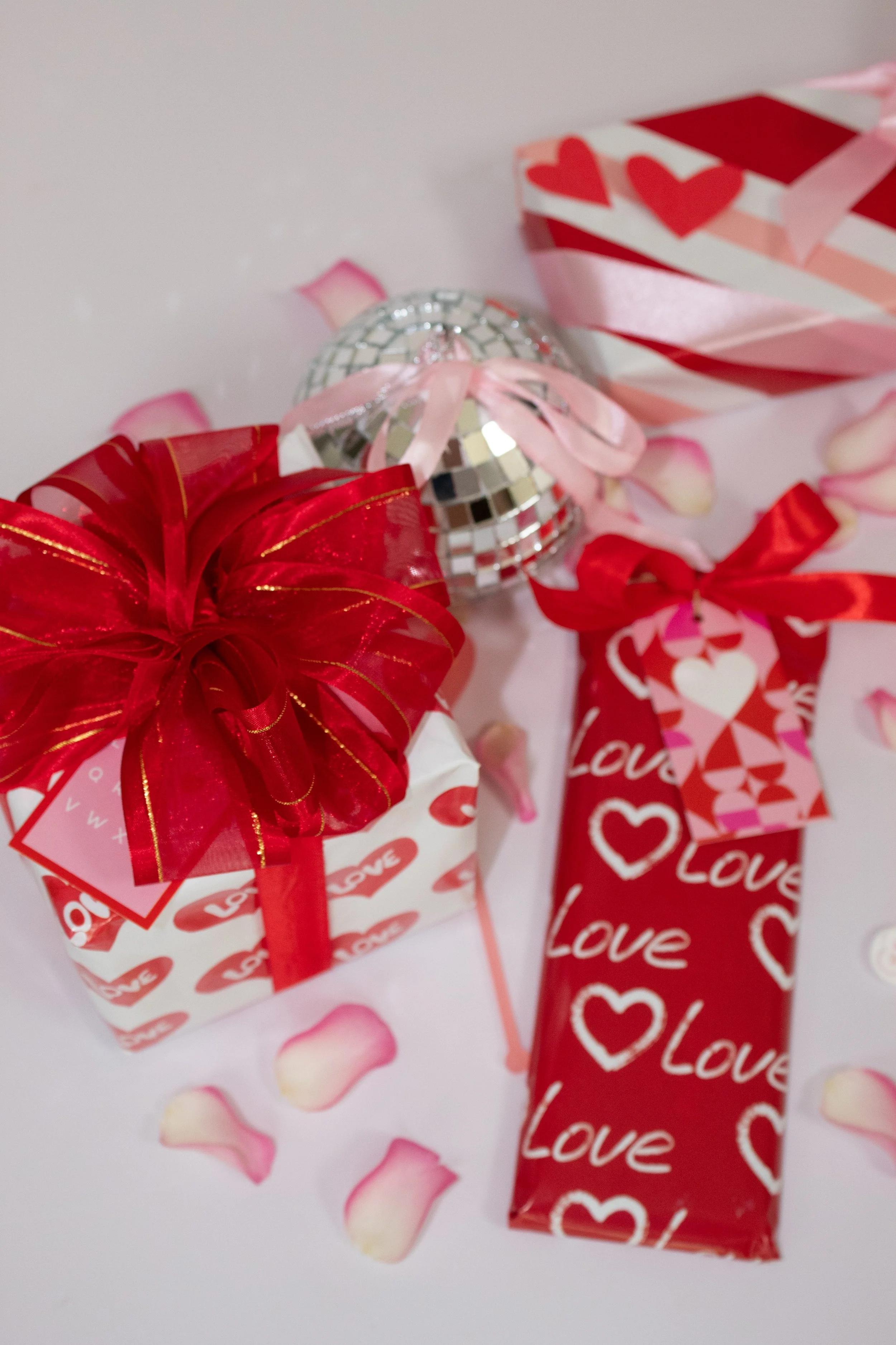 Valentine's Day-themed gifts including a small white box with red hearts and the word 'Love' wrapped with a red ribbon, a red gift bag with white 'Love' and heart patterns | Luxury Gift Wrapping & Custom Hampers