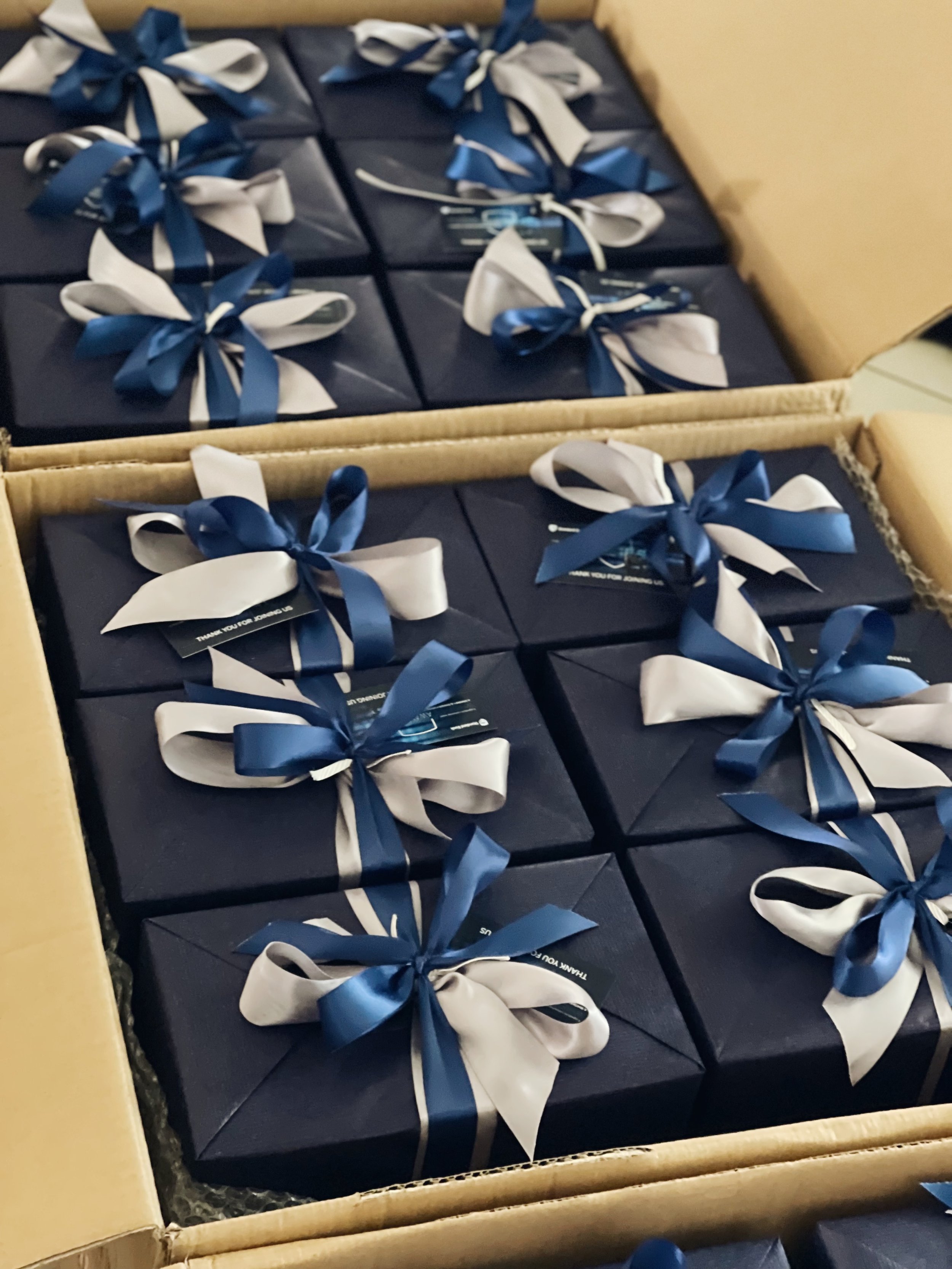 Multiple navy blue gift boxes wrapped with white and navy blue ribbons inside a cardboard box | Luxury Gift Wrapping & Custom Hampers