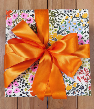 A gift box wrapped in floral patterned paper with a large orange satin ribbon tied in a bow | Luxury Gift Wrapping & Custom Hampers