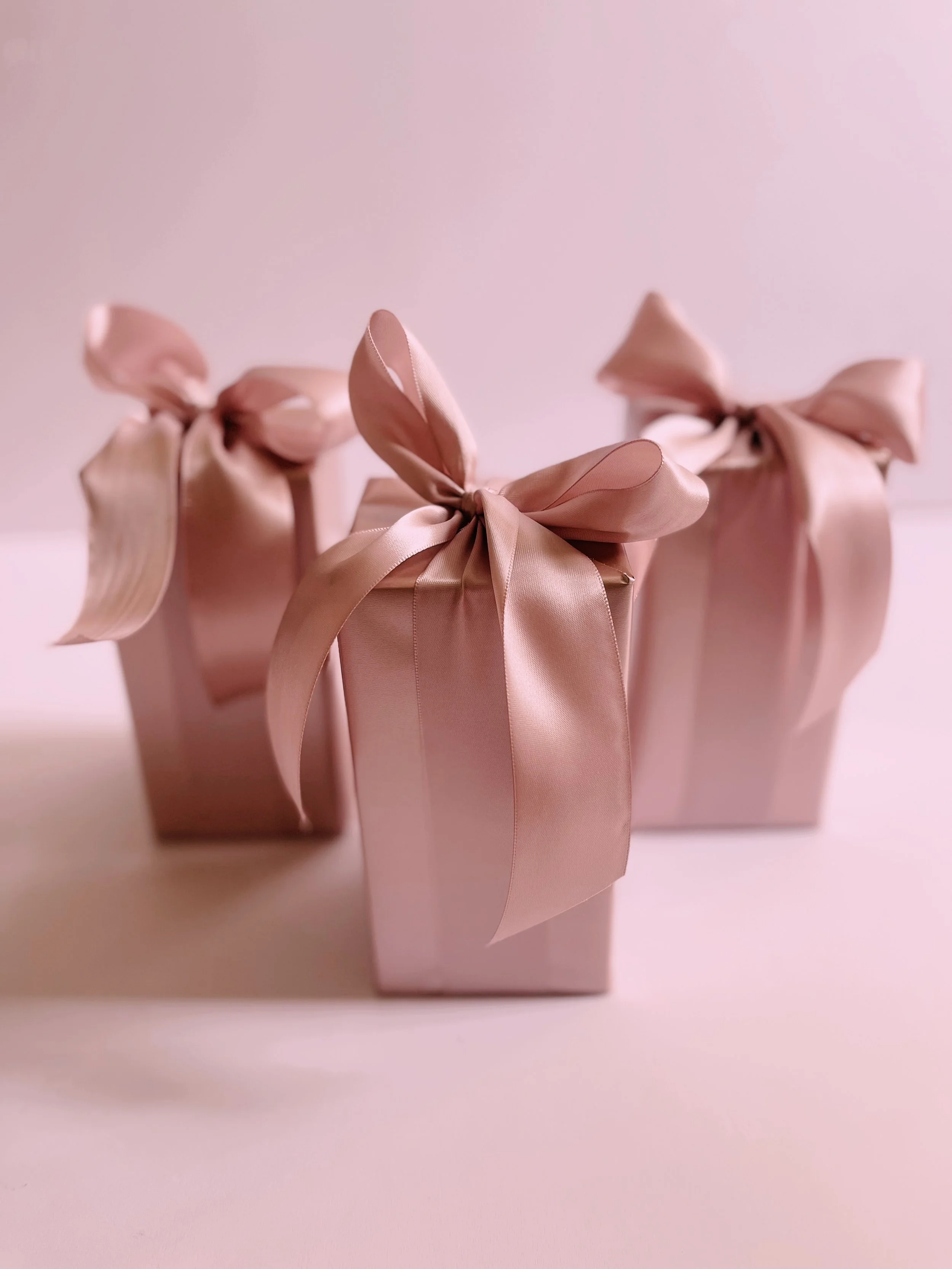 Three pink gift boxes wrapped with satin ribbons tied in bows | Luxury Gift Wrapping & Custom Hampers