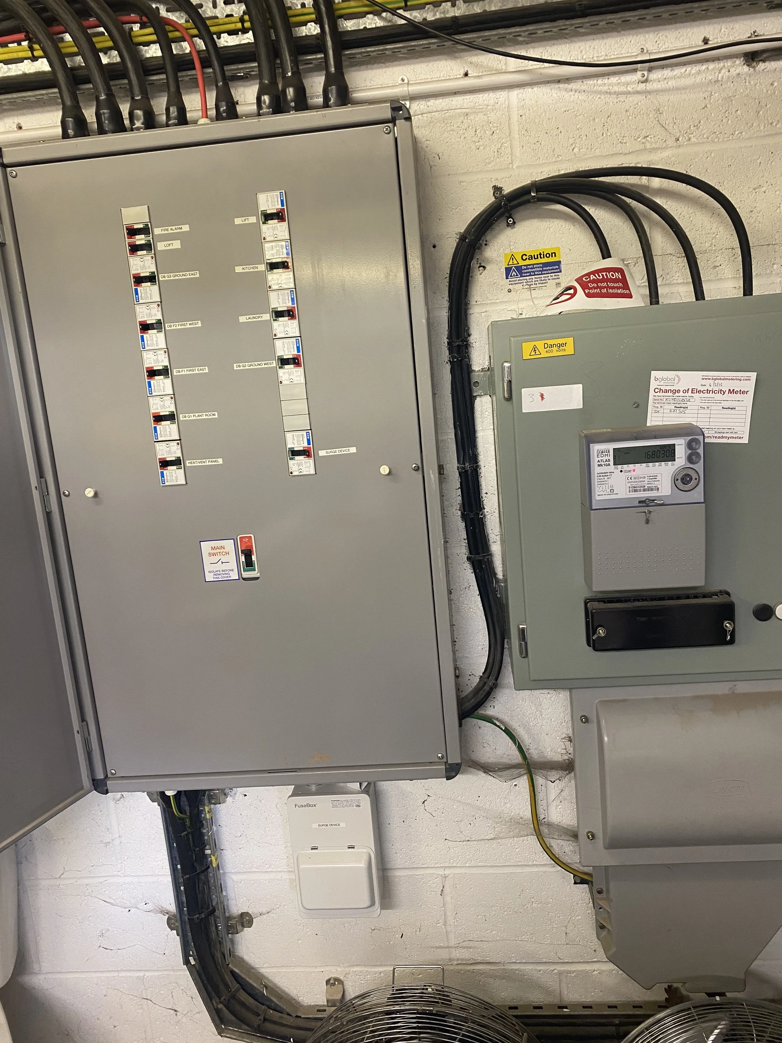Electrical control panels and meters mounted on a white brick wall in an industrial or maintenance room.