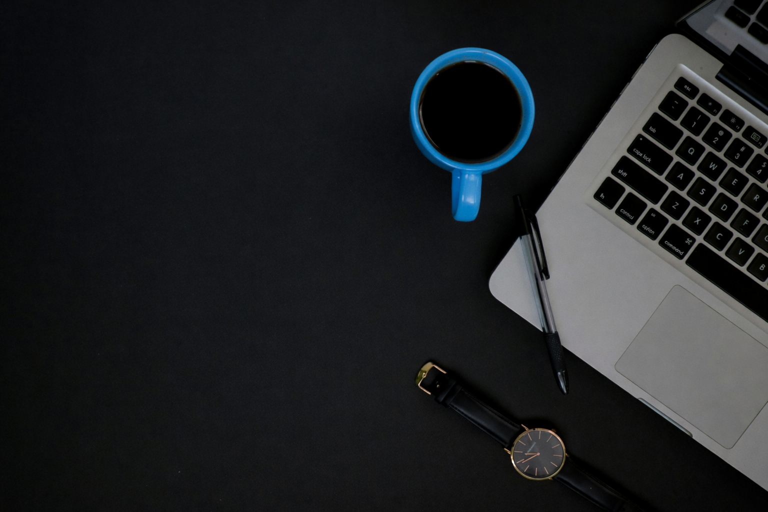 Foto bianco nero con pc, penna, orologio sul tavolo e tazzina blu unico elemento colorato
