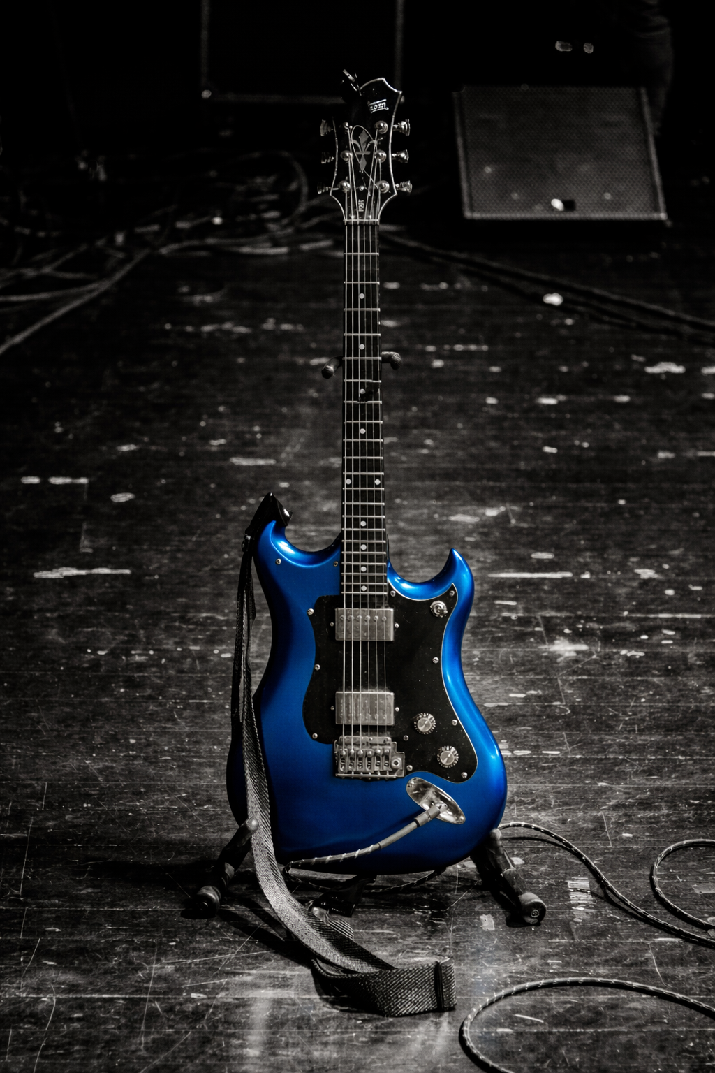 Chitarra elettrica blu luccicante su cavalletto su palco e ambientazione scura