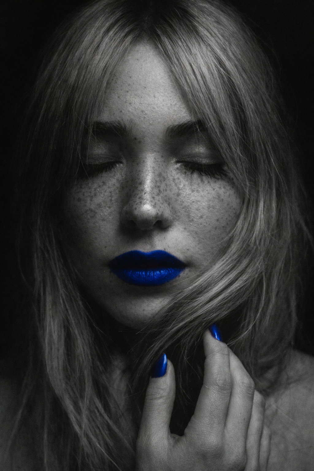 Ritratto donna con lentiggini occhi chiusi bianco e nero; rossetto e smalto blu acceso, unici punti colorati